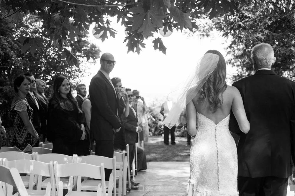 Black and white of bride and her father walking down the aisle during ceremony at the vine hill house