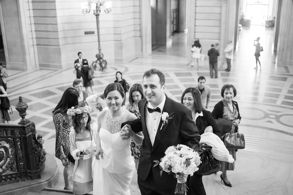 Black and white photo of bride and groom climbing grand staircase at San Francisco City Hall