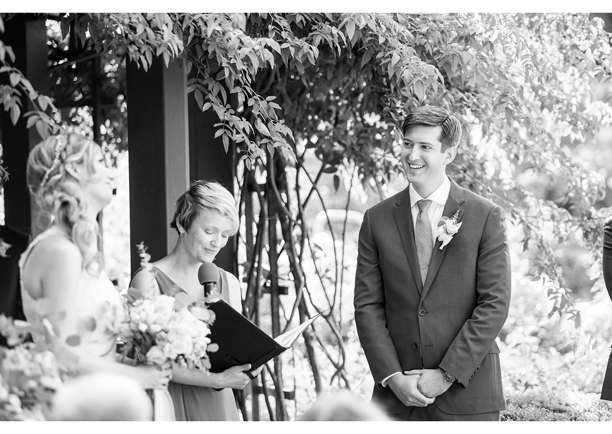 Black and white photo of groom smiling at his bride during wedding ceremony