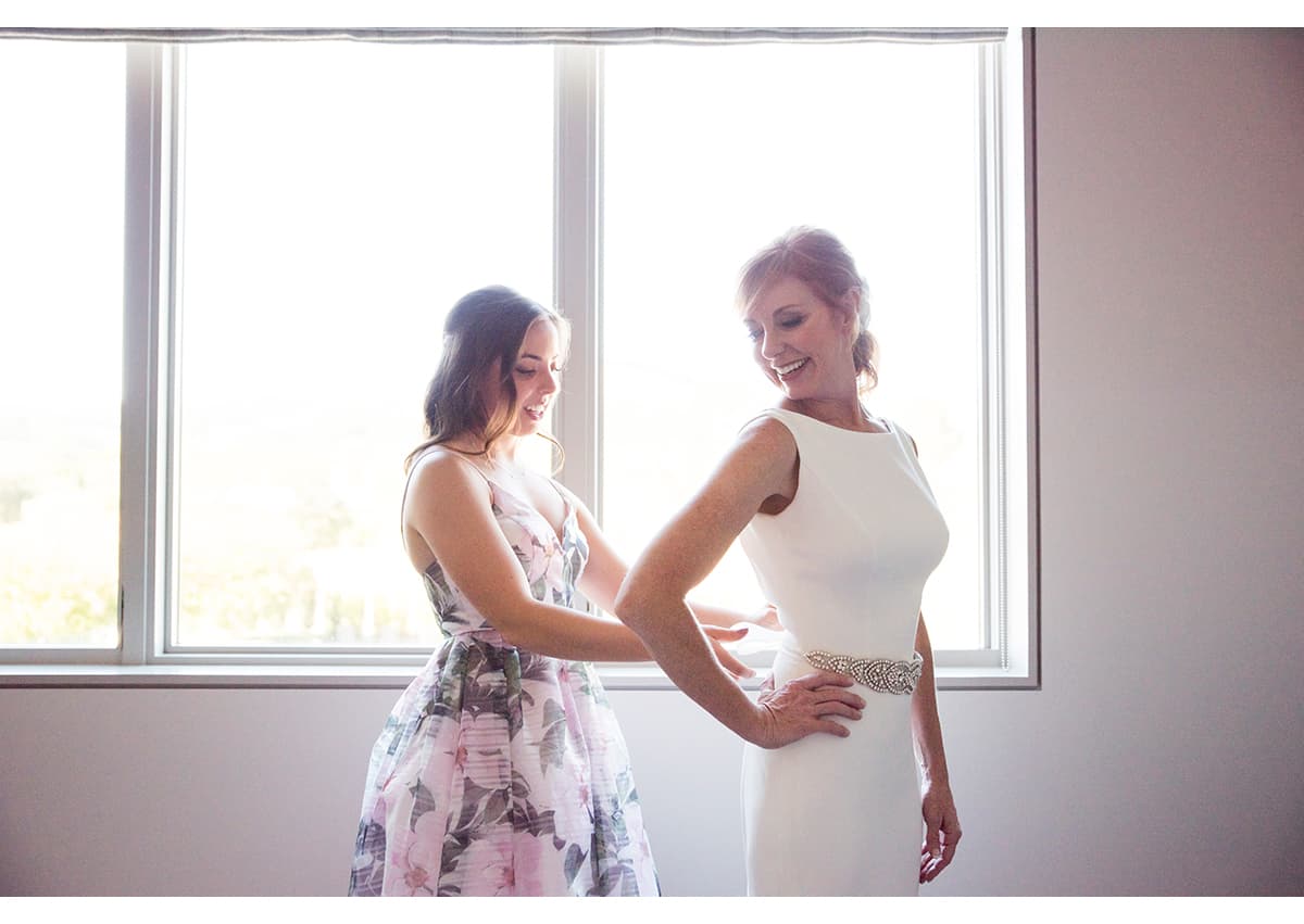 Daughter of bride helping mother with wedding dress