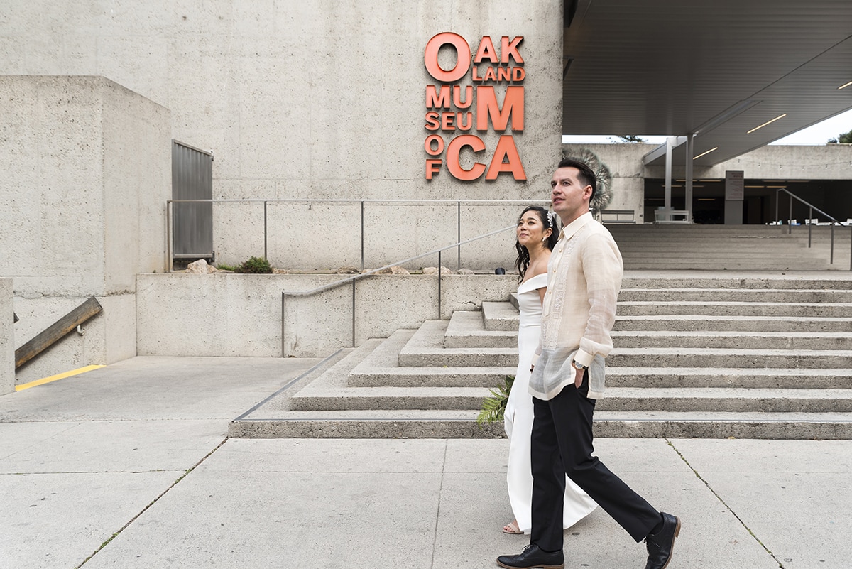 Bride and Groom walking with Oakland Museum in background