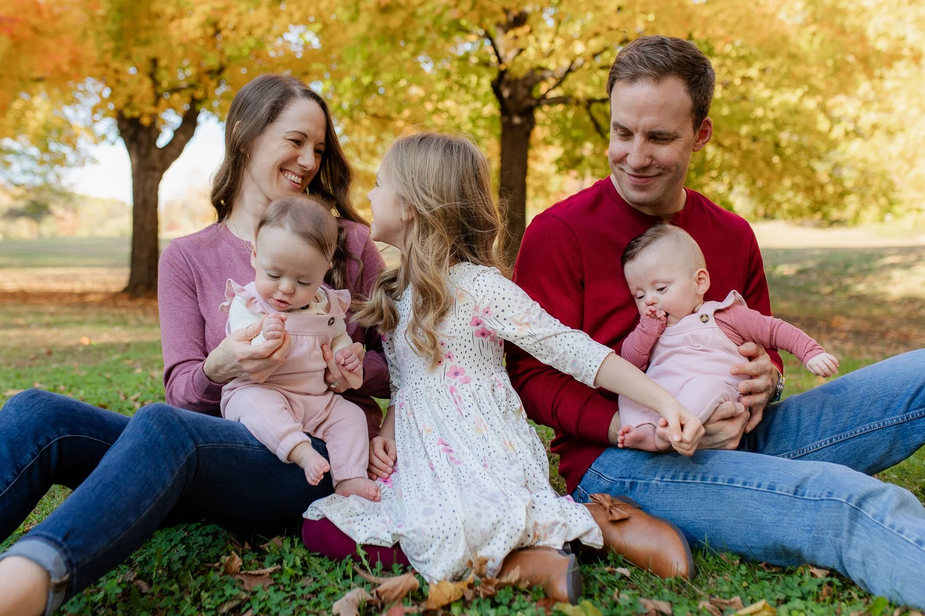 Family of 5 sitting on grass under bright yellow trees