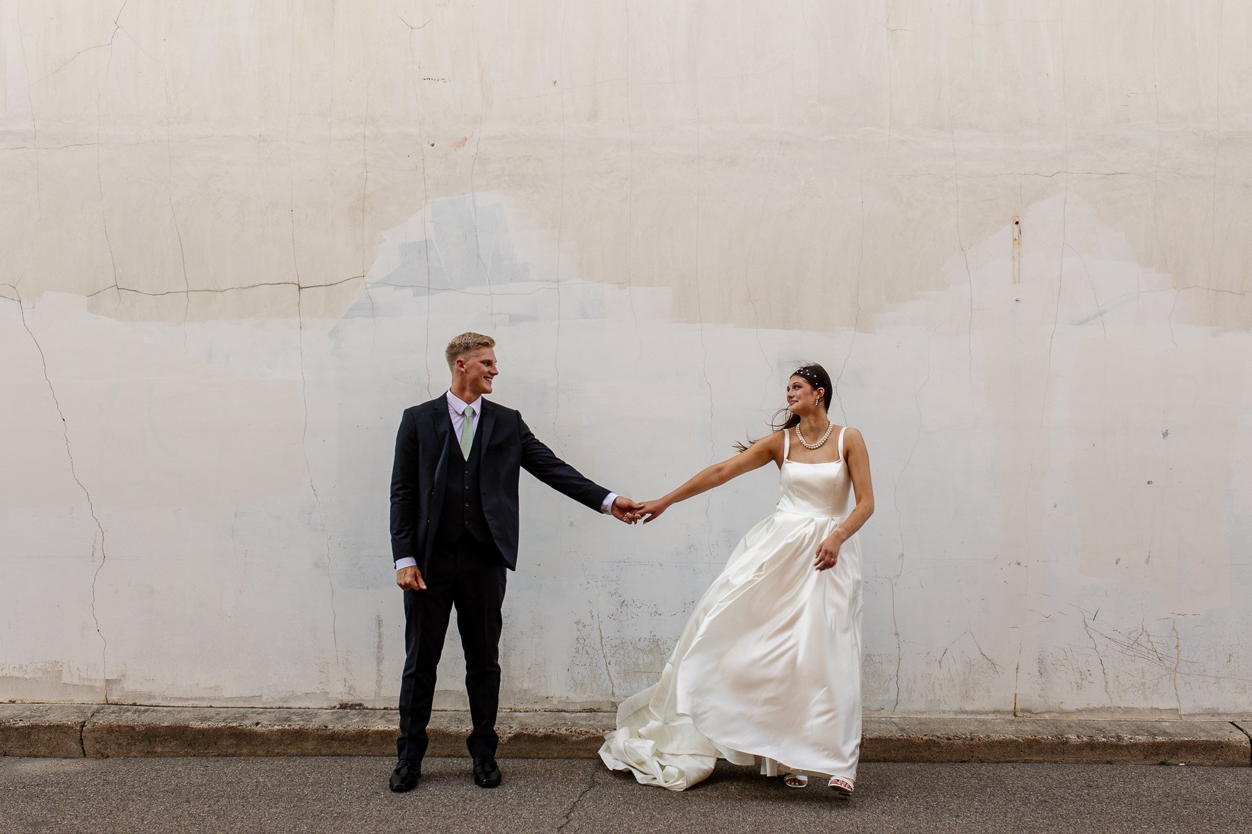 bride and groom standing in front of a white wall holding hands