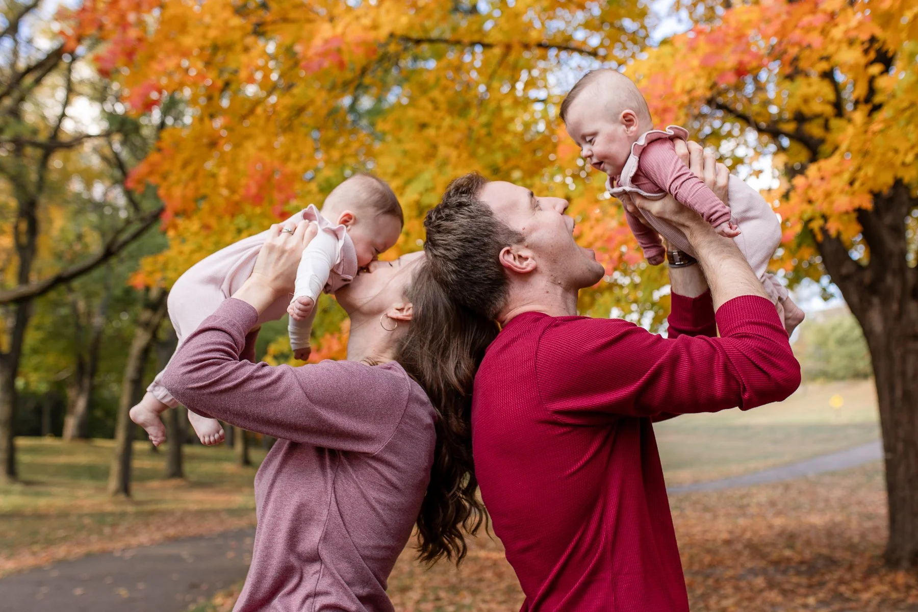 Parents holding up twin girls against background of yellow trees
