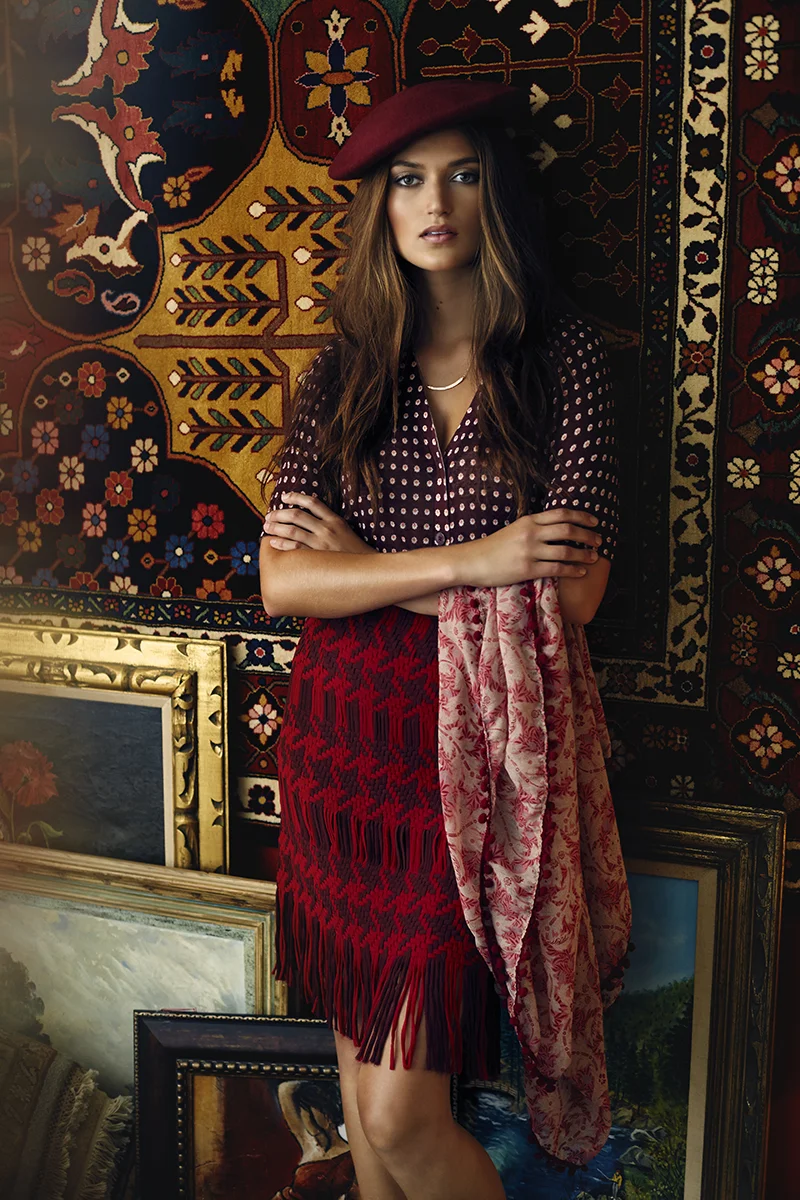  St. Paul editorial styling featuring woman in red and purple patterned skirt, cardigan, and beret with ornate rug backdrop and moody aesthetic 