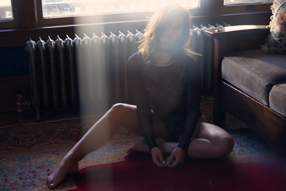  Editorial fashion styling by Minneapolis wardrobe stylist featuring model in lace onesie with moody natural light and ornate rug 