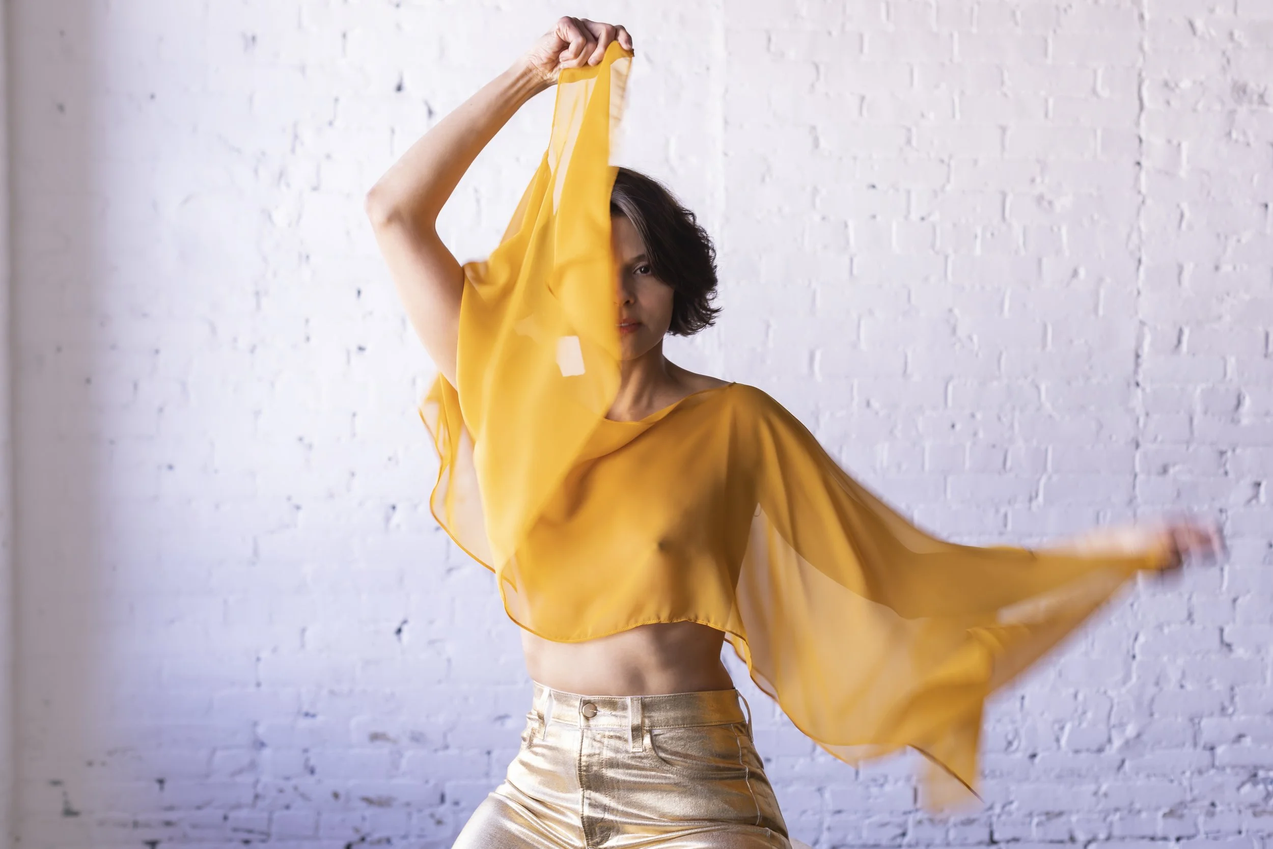  New York fashion, trend consultant and editorial stylist featuring model in whimsical sheer orange top and gold pants, posed with fabric over eye 