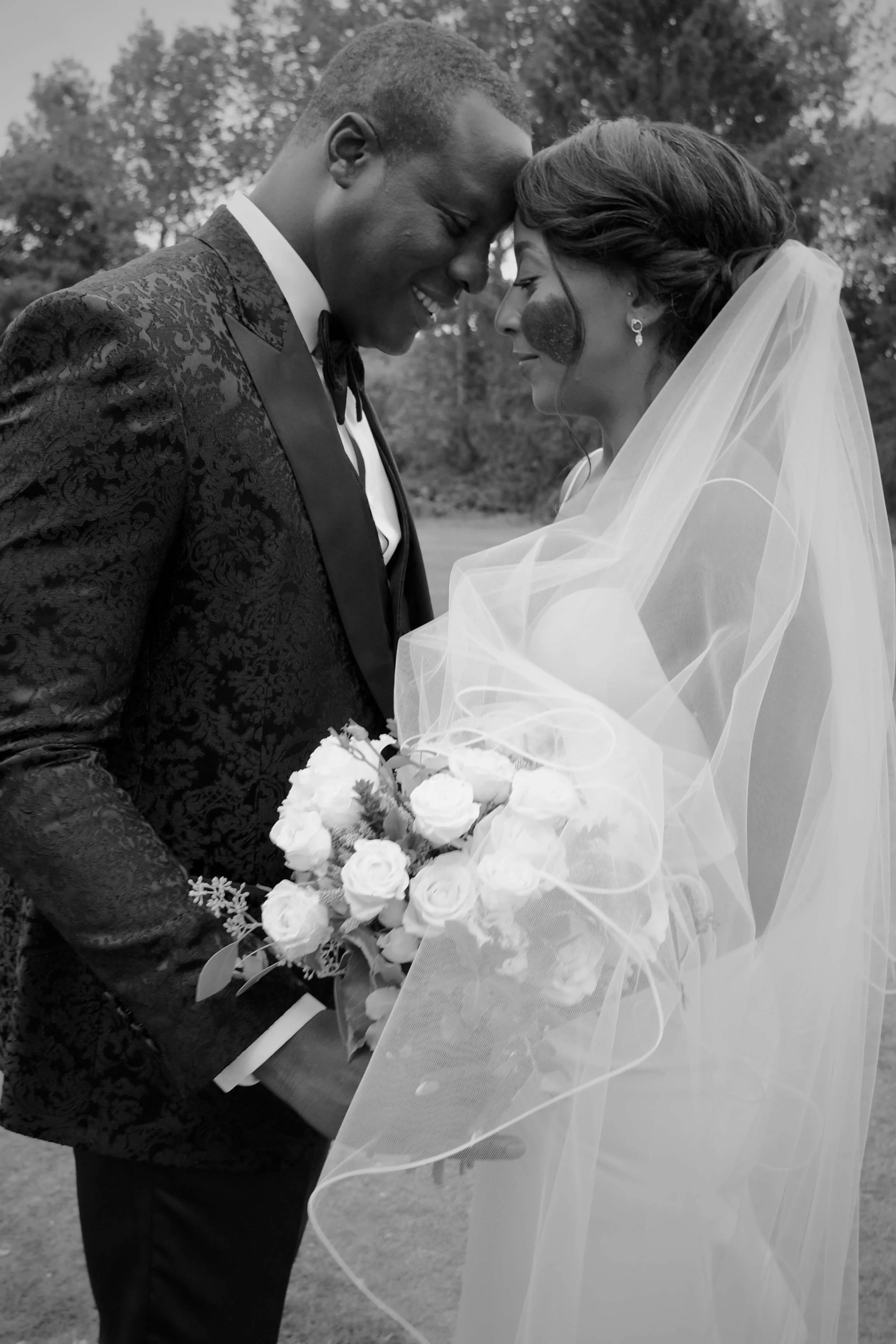A romantic black and white wedding portrait of the bride and groom sharing an intimate moment, captured beautifully with her bridal bouquet of roses.