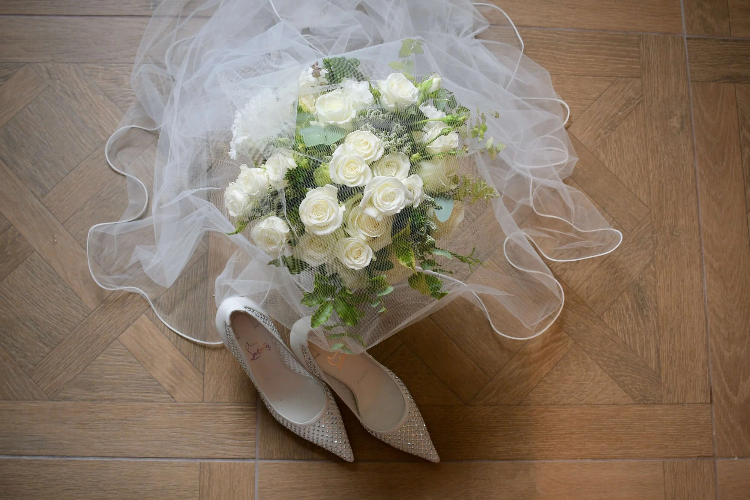 Bridal bouquet of white roses with greenery, wedding veil, and Christian Louboutin bridal shoes styled together — wedding details photography.