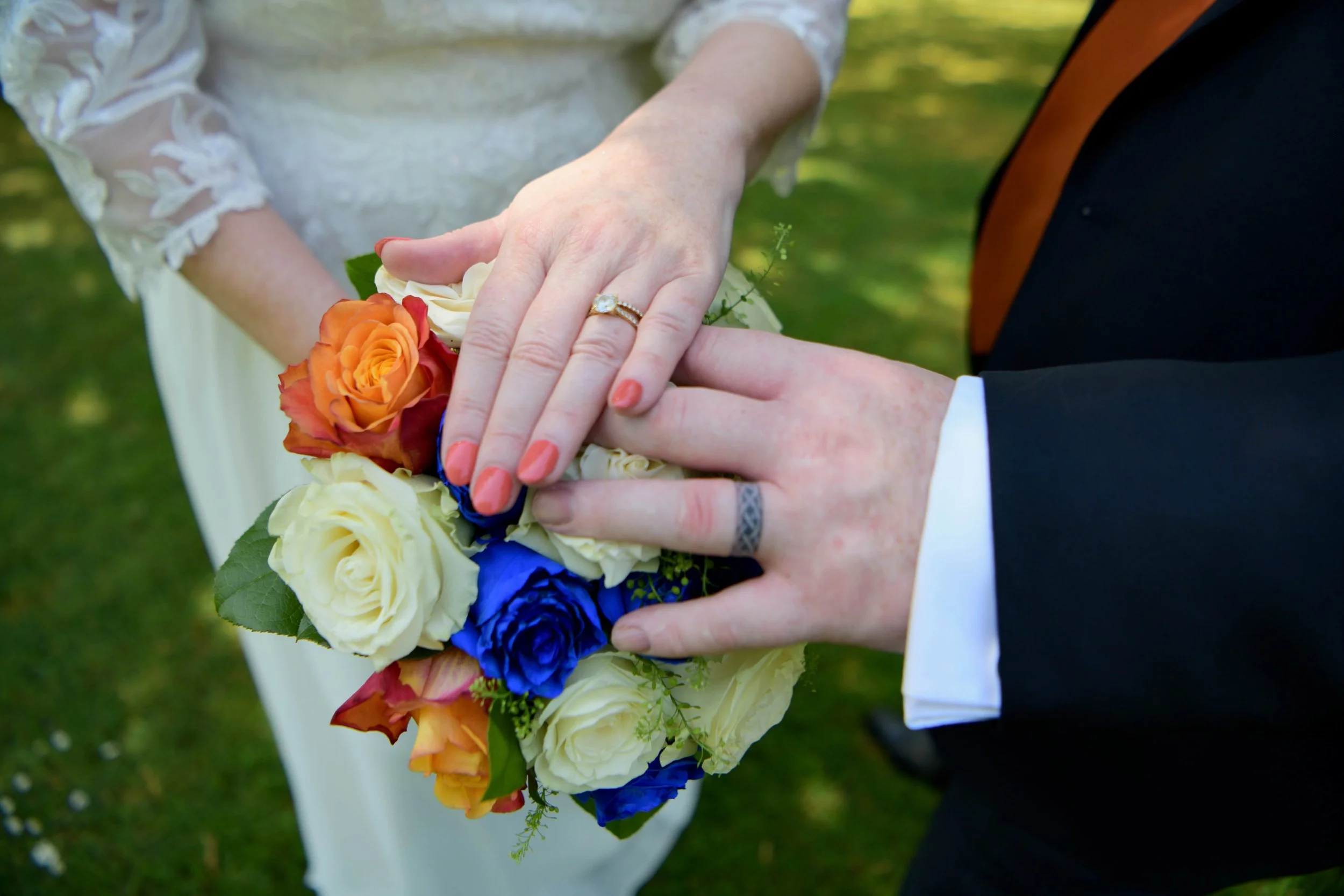 Bride and groom displaying their wedding rings over a colorful rose bouquet, captured in a romantic outdoor wedding photography portrait.