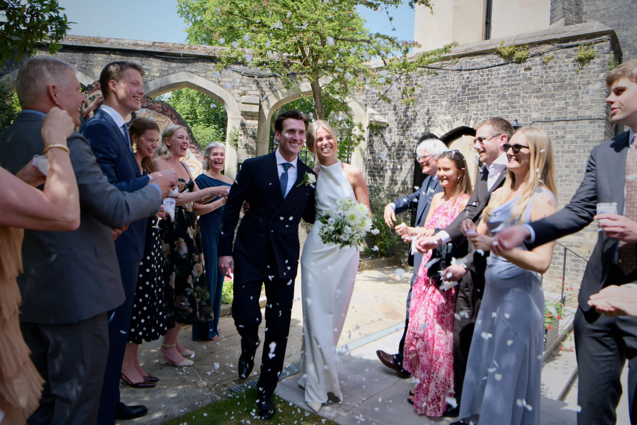 Joyful wedding celebration in London as the newlywed couple walk through confetti surrounded by smiling guests, capturing elegant, candid, and timeless luxury wedding photography.
