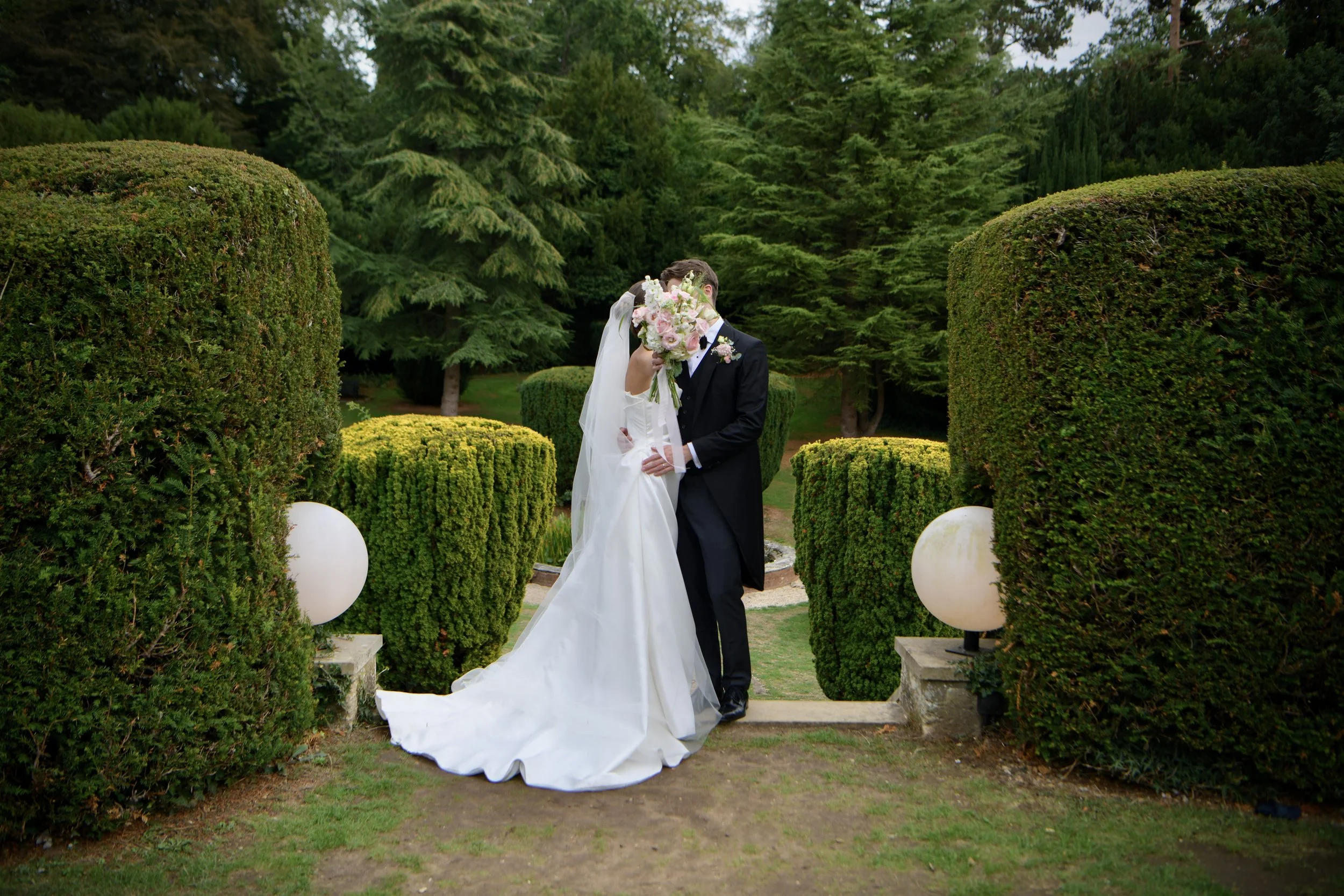 London wedding photographer capturing newlyweds kissing among beautifully manicured gardens and topiary 