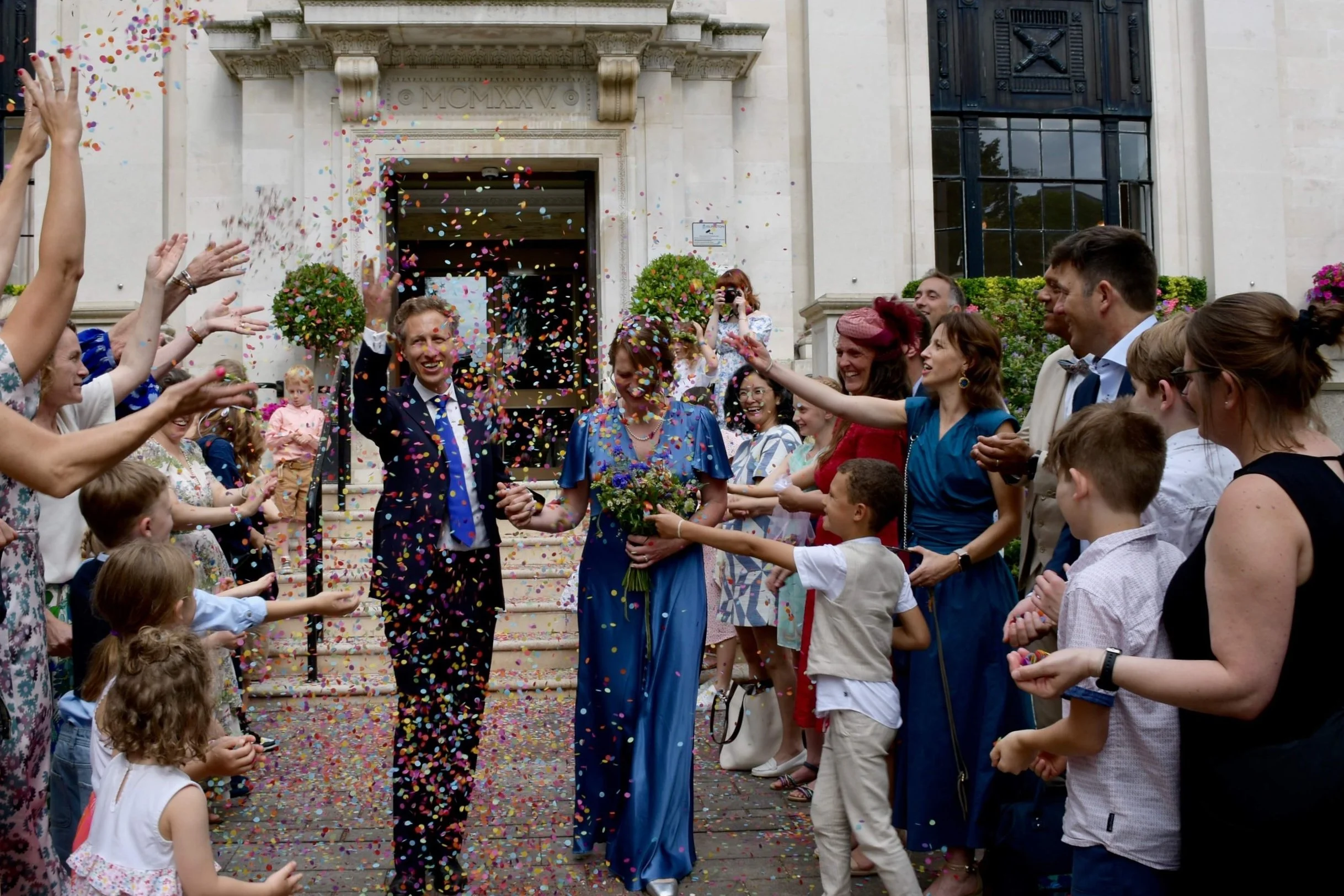 Joyful wedding moment as the couple exits ceremony with guests throwing confetti, captured in documentary-style photography.