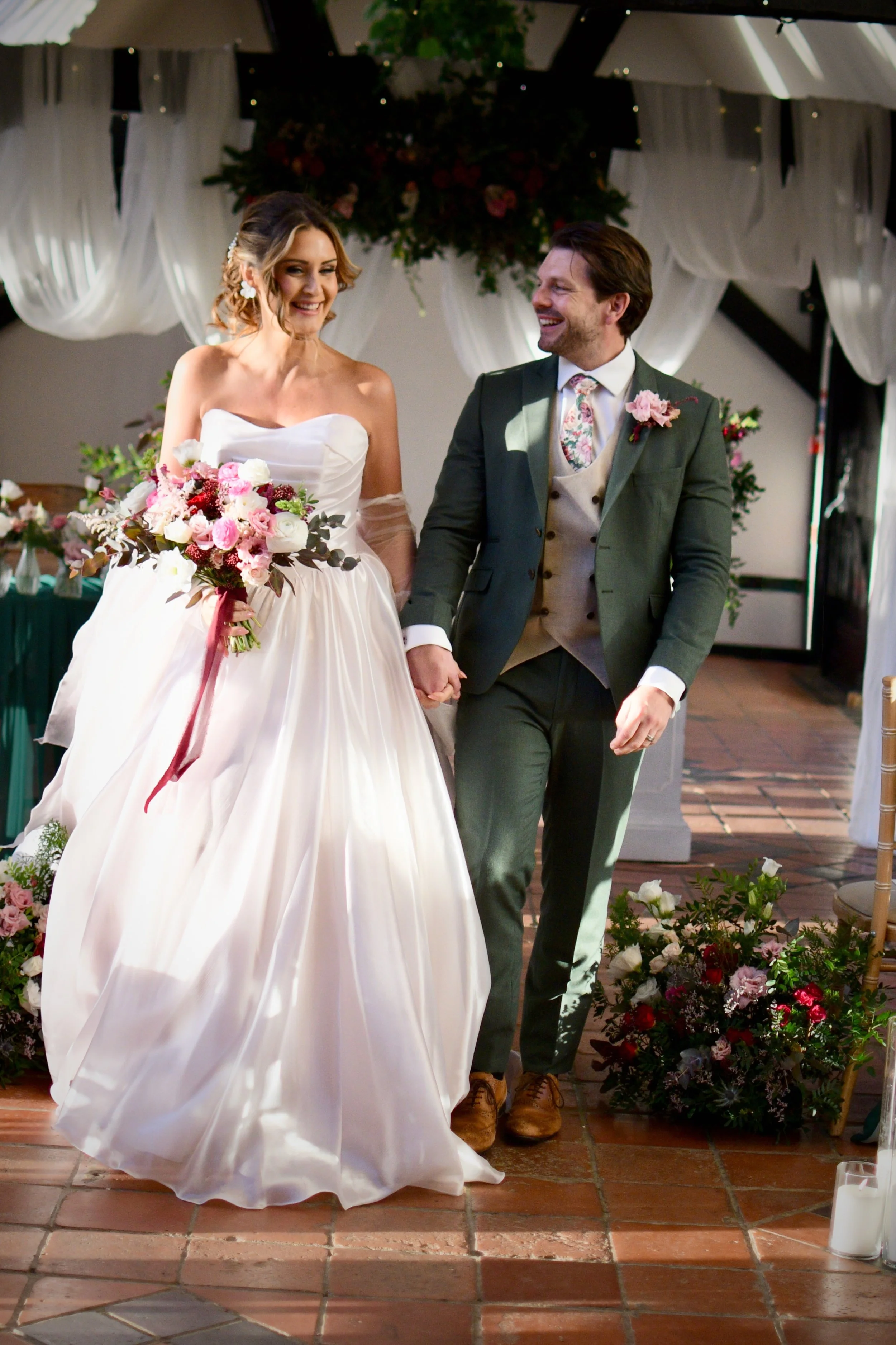 Bride and groom walking hand-in-hand down the aisle with bouquet and flowing wedding dress