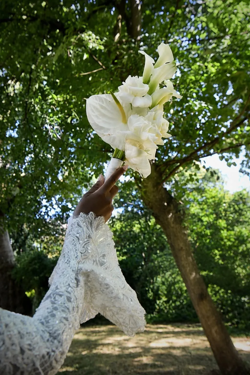 Bride holding a white wedding bouquet beneath green trees during a London wedding, photographed in natural light.