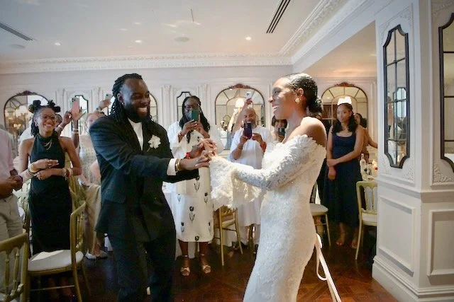 Bride and groom dancing together during their wedding reception in London, surrounded by smiling family and friends capturing the joyful moment on their phones.
