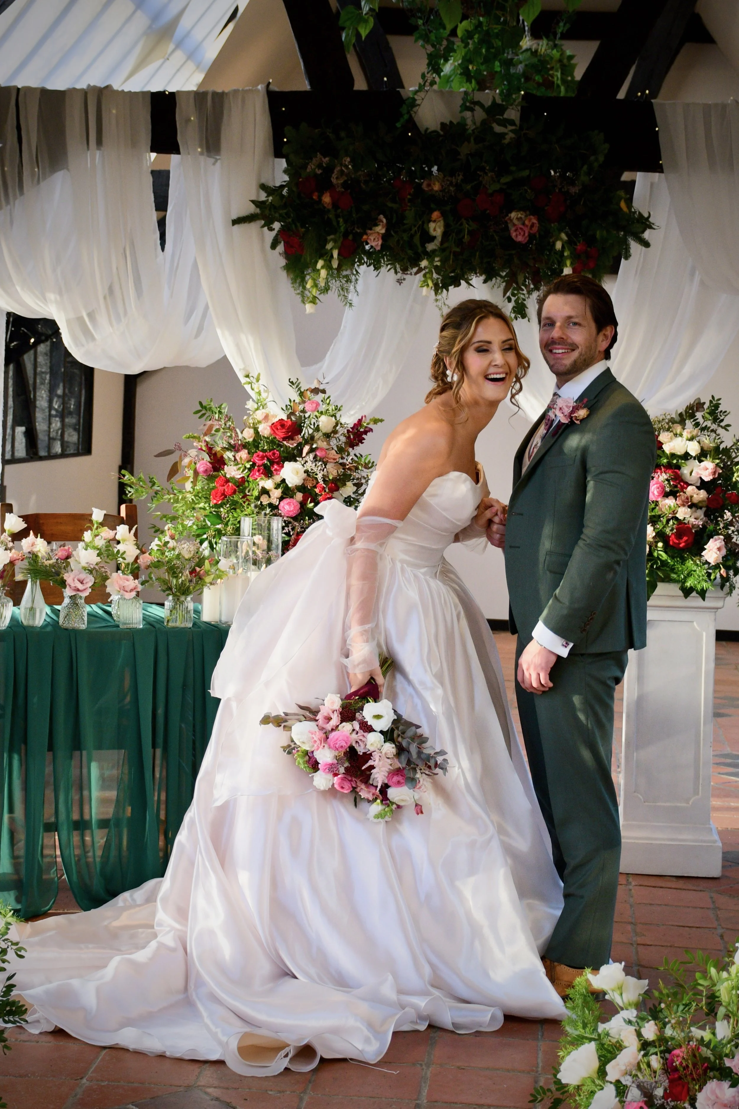 Laughing bride and groom standing among elegant floral wedding décor during their indoor ceremony