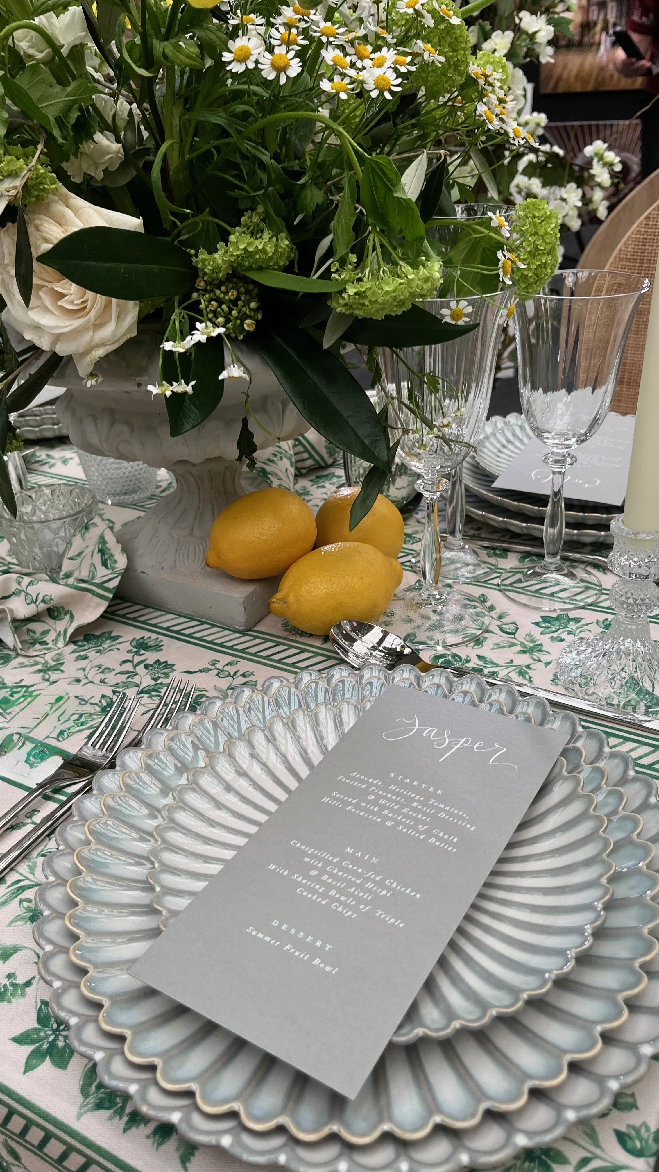 Elegant wedding tablescape with fresh white and green florals, citrus accents, and fine glassware, styled with a modern menu card and textured charger plate—perfect inspiration for timeless, romantic wedding receptions.