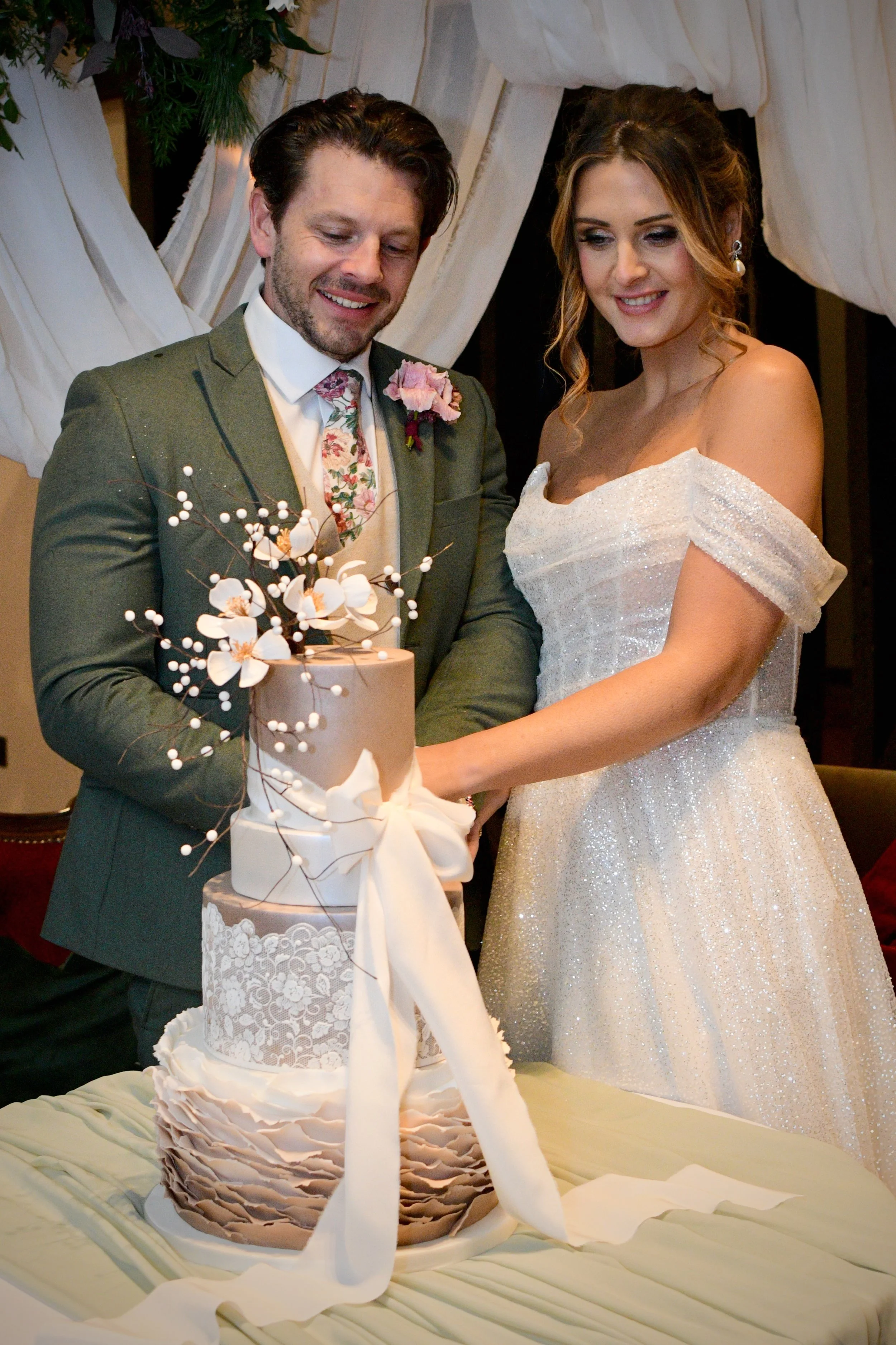 Couple cutting an elegant tiered wedding cake decorated with flowers.
