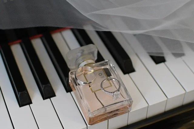 Engagement and wedding rings on perfume bottle resting on piano, veil next to it 