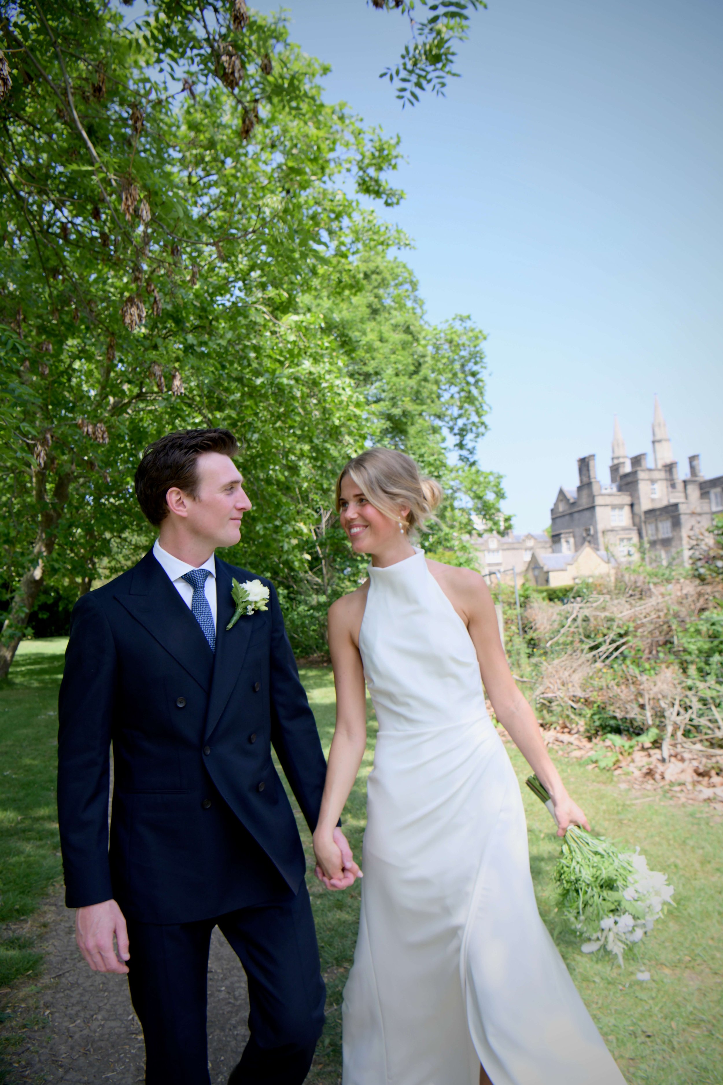 Romantic outdoor wedding portrait of a newlywed couple walking hand in hand through the beautiful London Regent’s Park, capturing elegant bridal style and timeless luxury wedding photography.