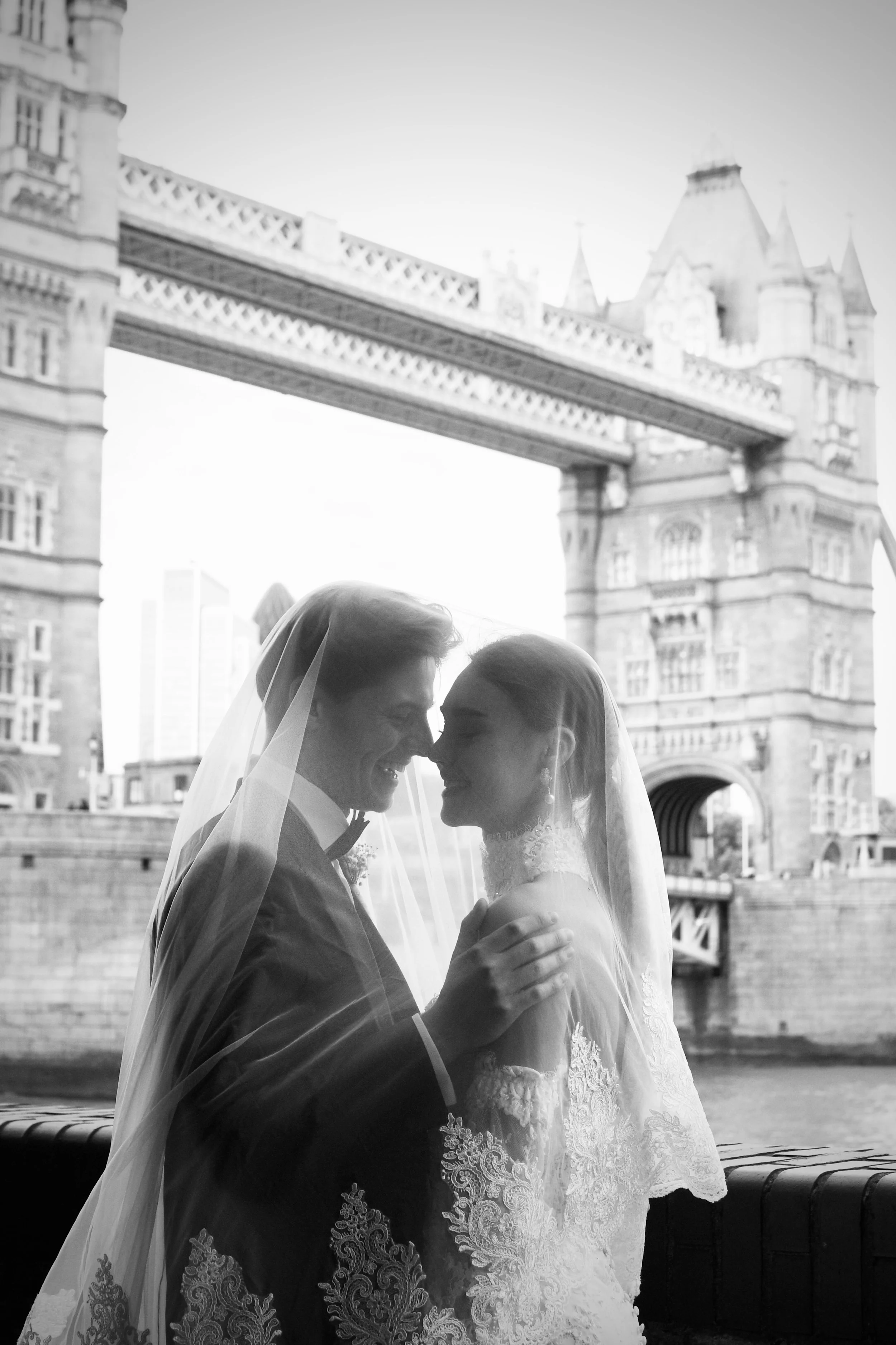 A romantic black and white wedding portrait of the bride and groom sharing an intimate moment and laughing by Tower Bridge, London 