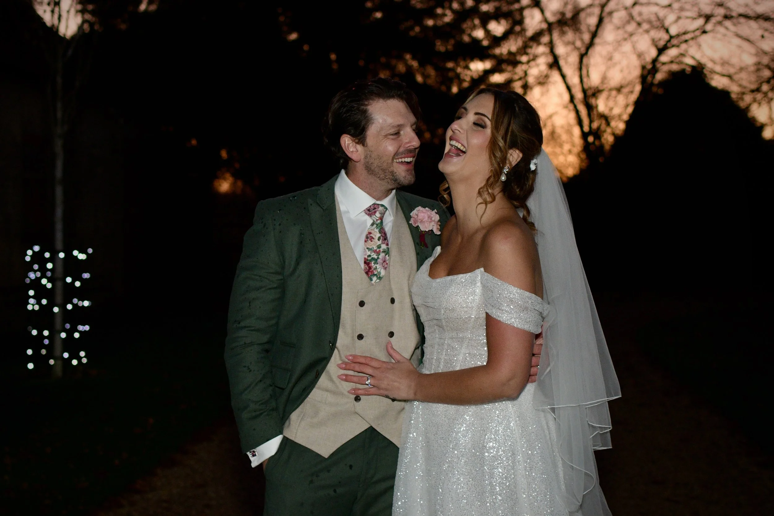 Bride and groom laughing together at sunset during their romantic outdoor wedding