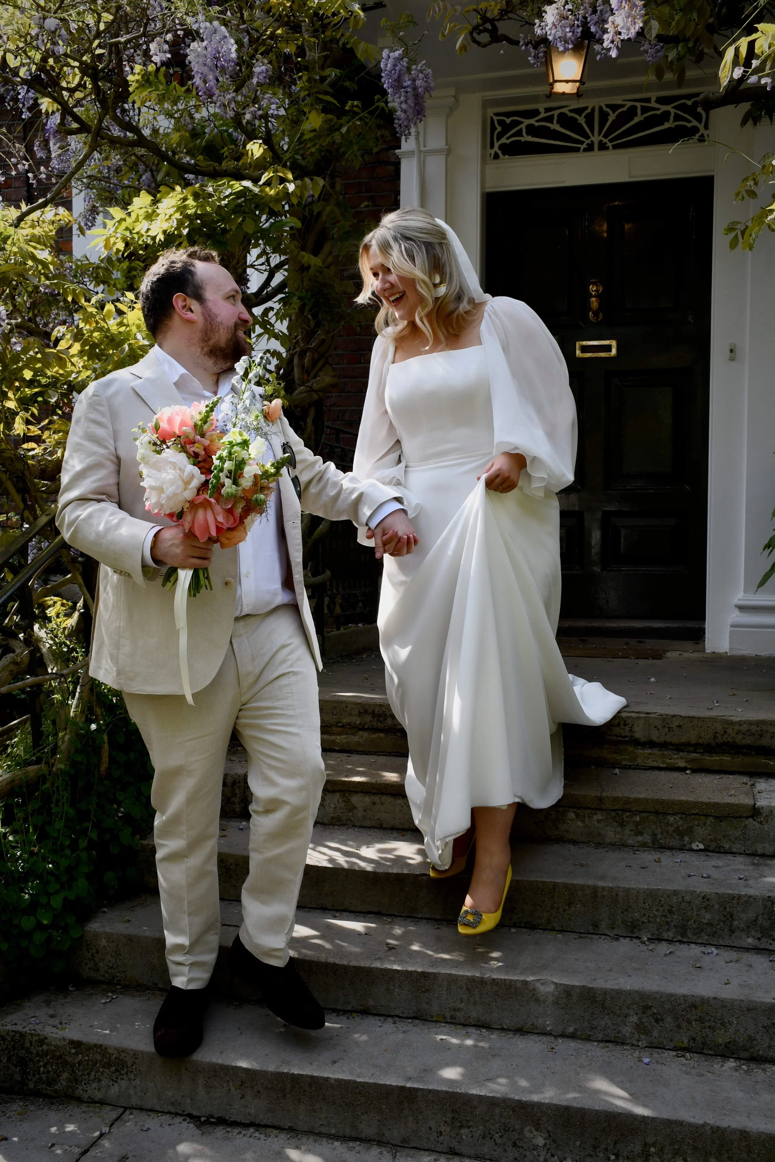 Modern bride and groom stepping into married life with style — the bride stuns in a square-neck gown and vibrant yellow Manolo Blahniks, hand in hand outside their charming London townhouse venue.
Keywords: London wedding photographer, candid weddin