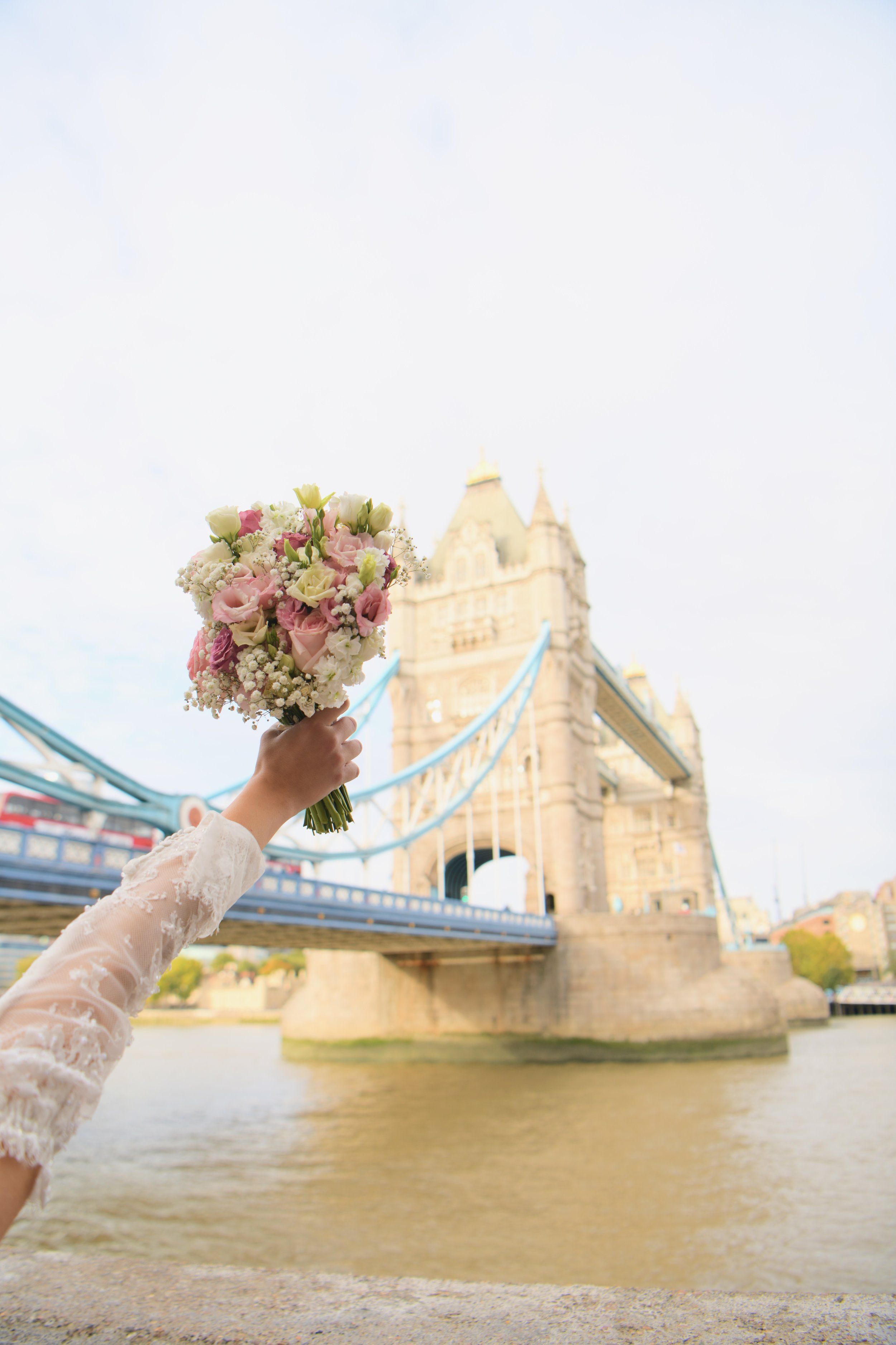 Bride raising her wedding bouquet by Tower Bridge, London