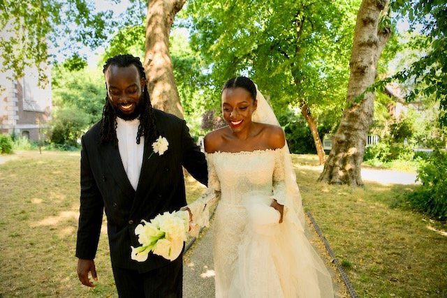 Bride and groom walking hand in hand through a garden after their London wedding ceremony, smiling and holding the bridal bouquet.