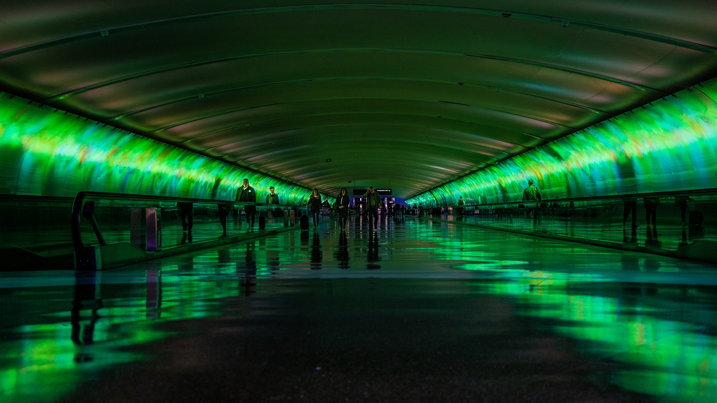 green-illuminated-transit-tunnel-with-travellators-and-people