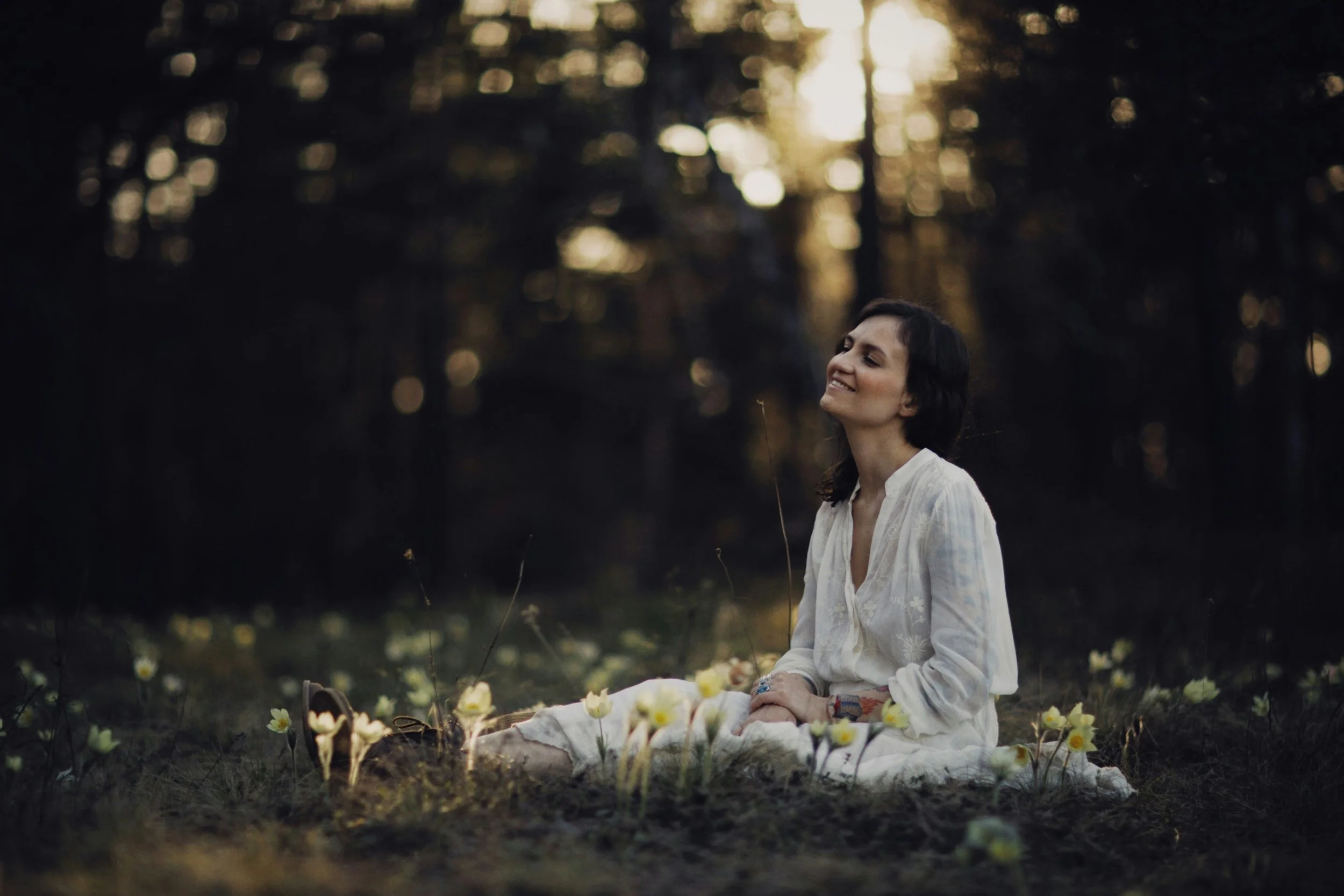 Woman sitting peacefully in field of flowers reflecting on childhood trauma patterns and healing