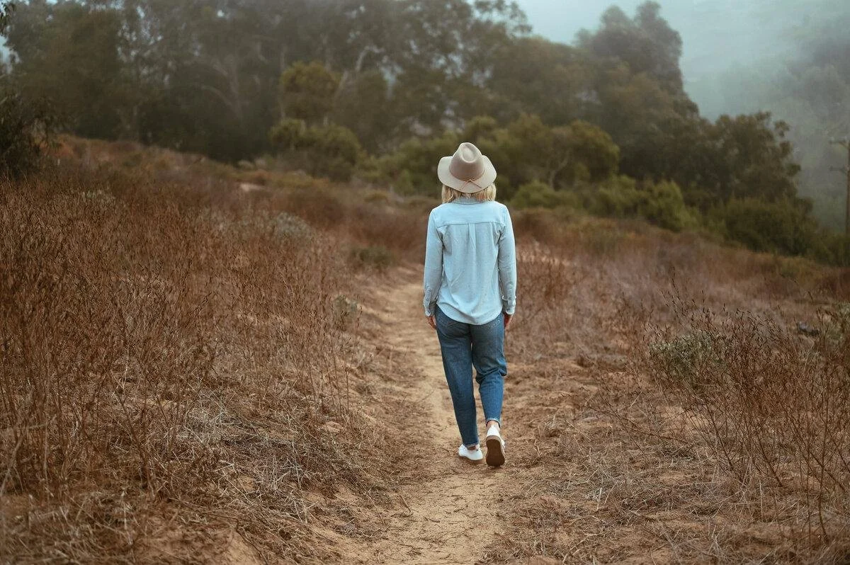 A woman wearing a hat walks alone through a sunlit field, symbolizing self-reflection, healing, and reconnecting with yourself after years of self-abandonment.