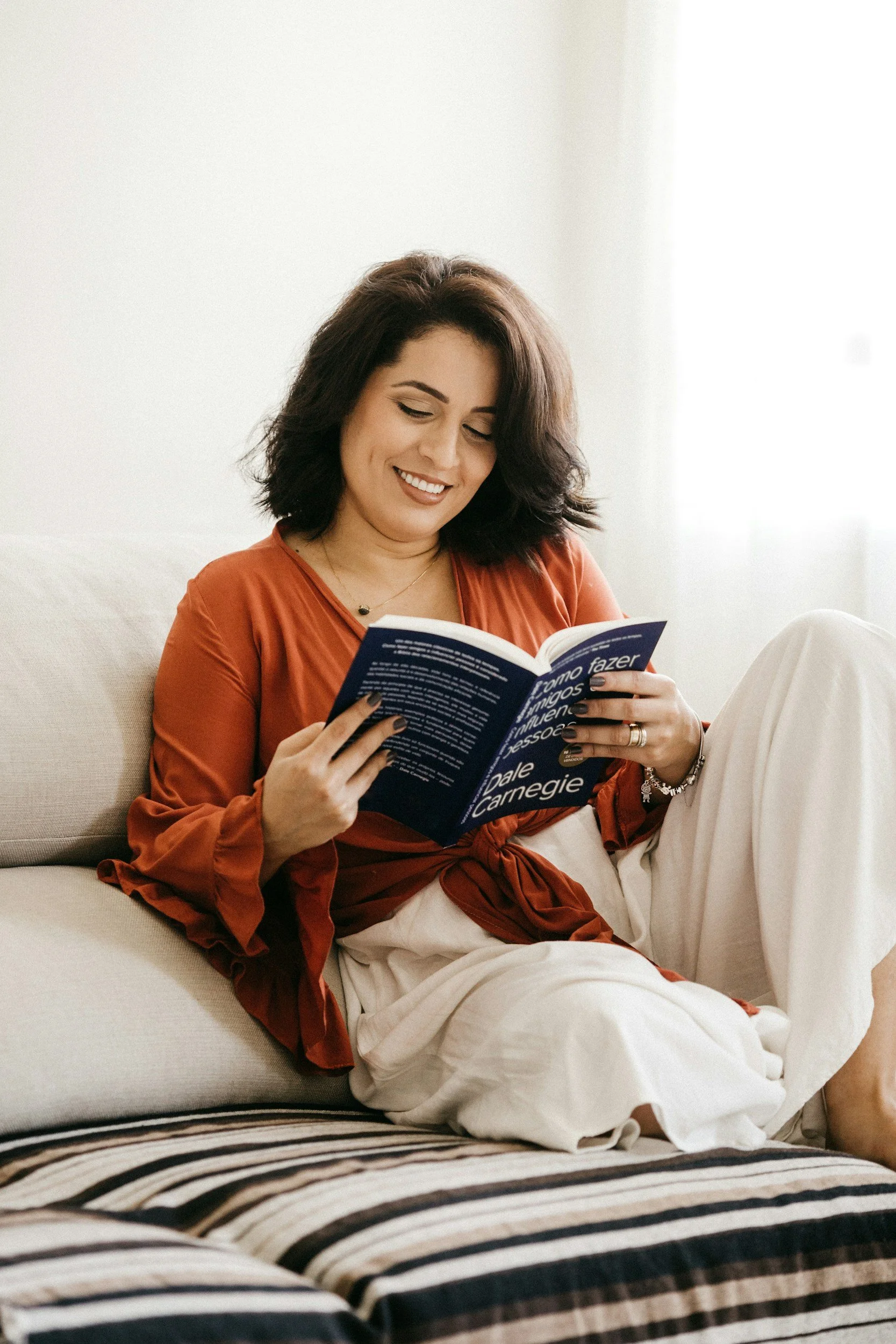A woman sits on her couch in a relaxed way reading a book