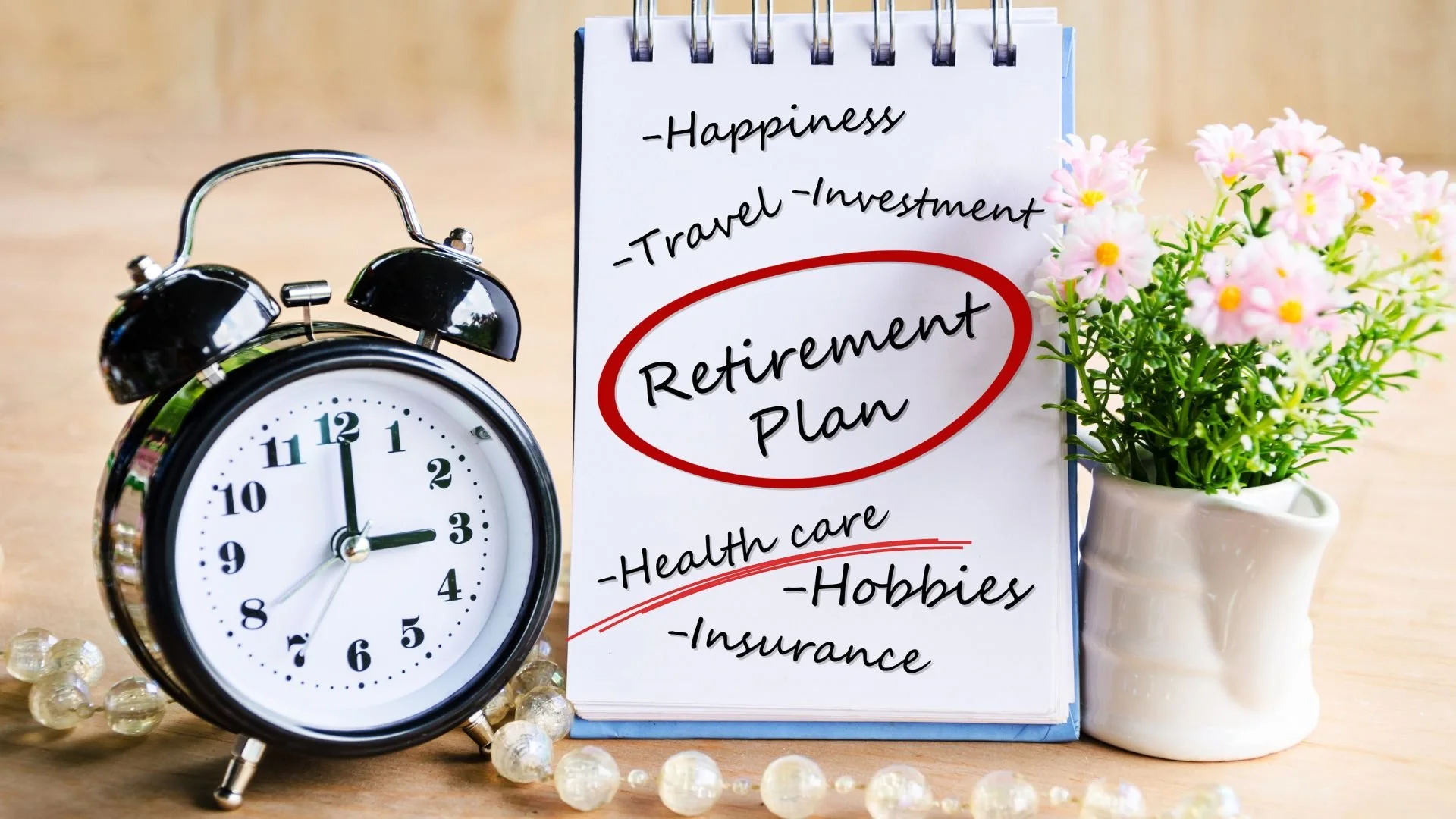On the left is an old fashioned alarm clock. Beside it is a notepad with happiness, travel, investment, retirement plan (circled in red), health care (underlined in red), hobbies and insurance.  Beside the notepad is a small bouquet of pink daisies
