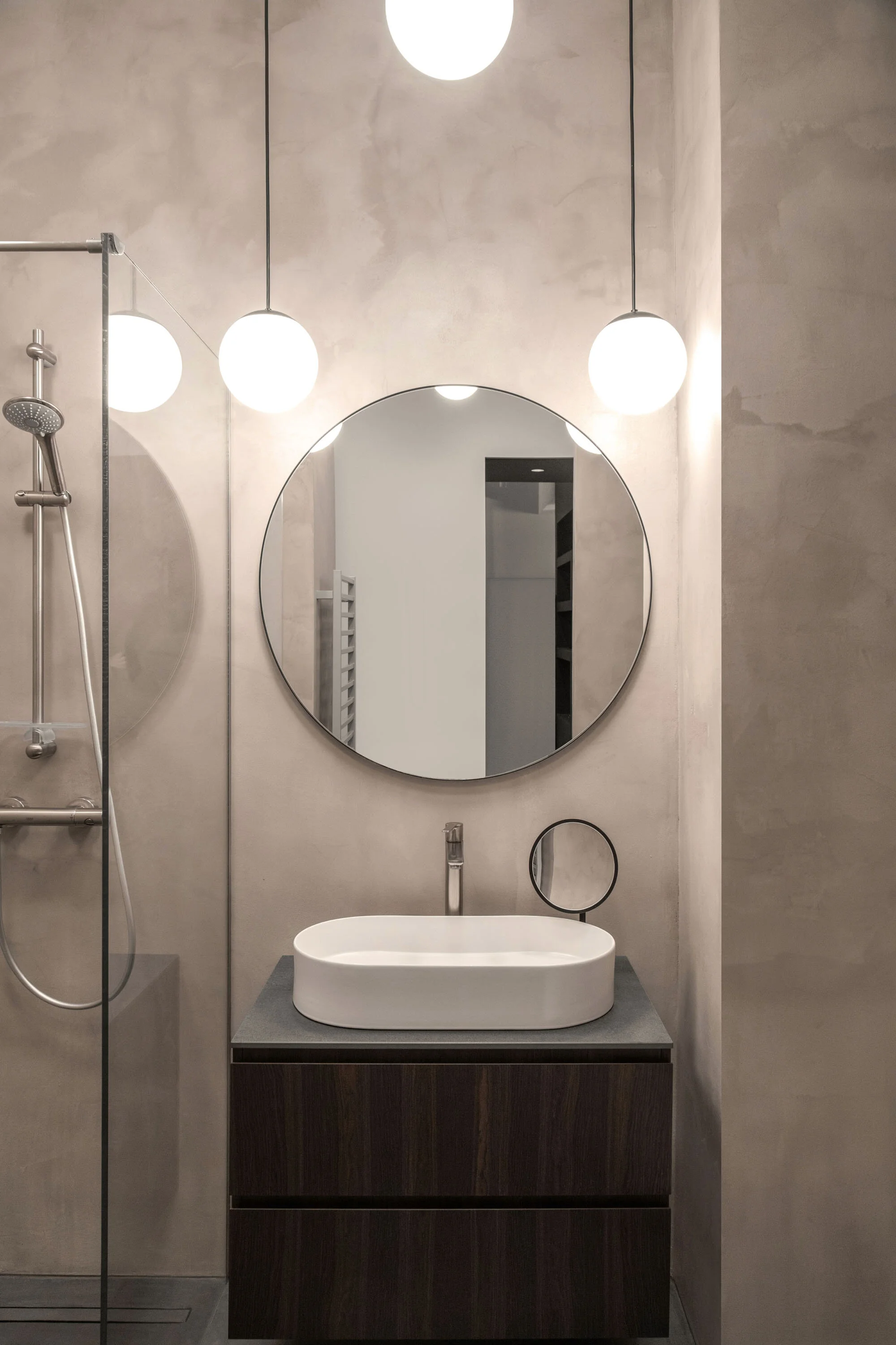 Salle de bains en béton ciré avec miroir rond sur l’Île de la Cité