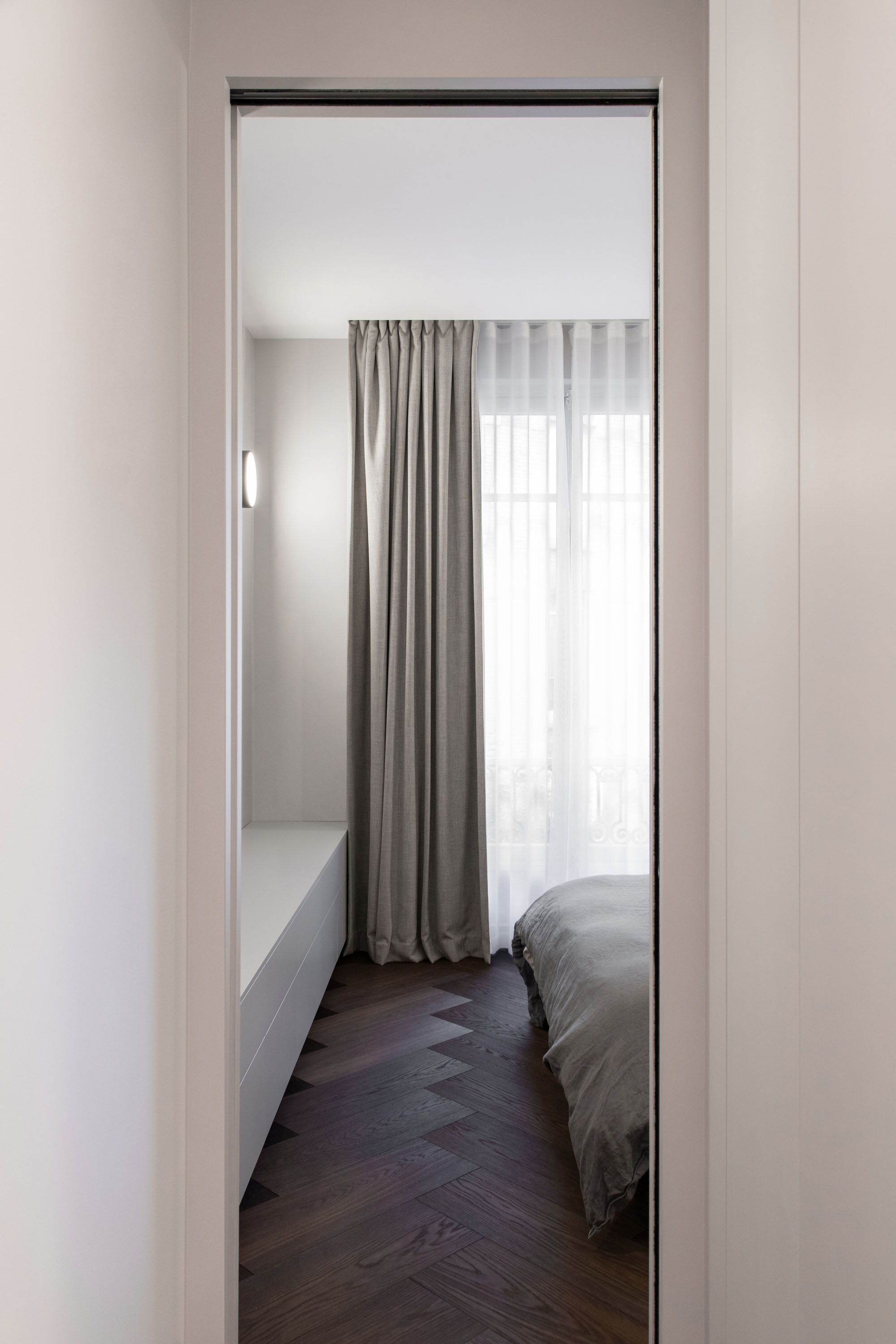 Chambre vue depuis le couloir d’un appartement rénové avec une porte coulissante et un parquet bauwerk