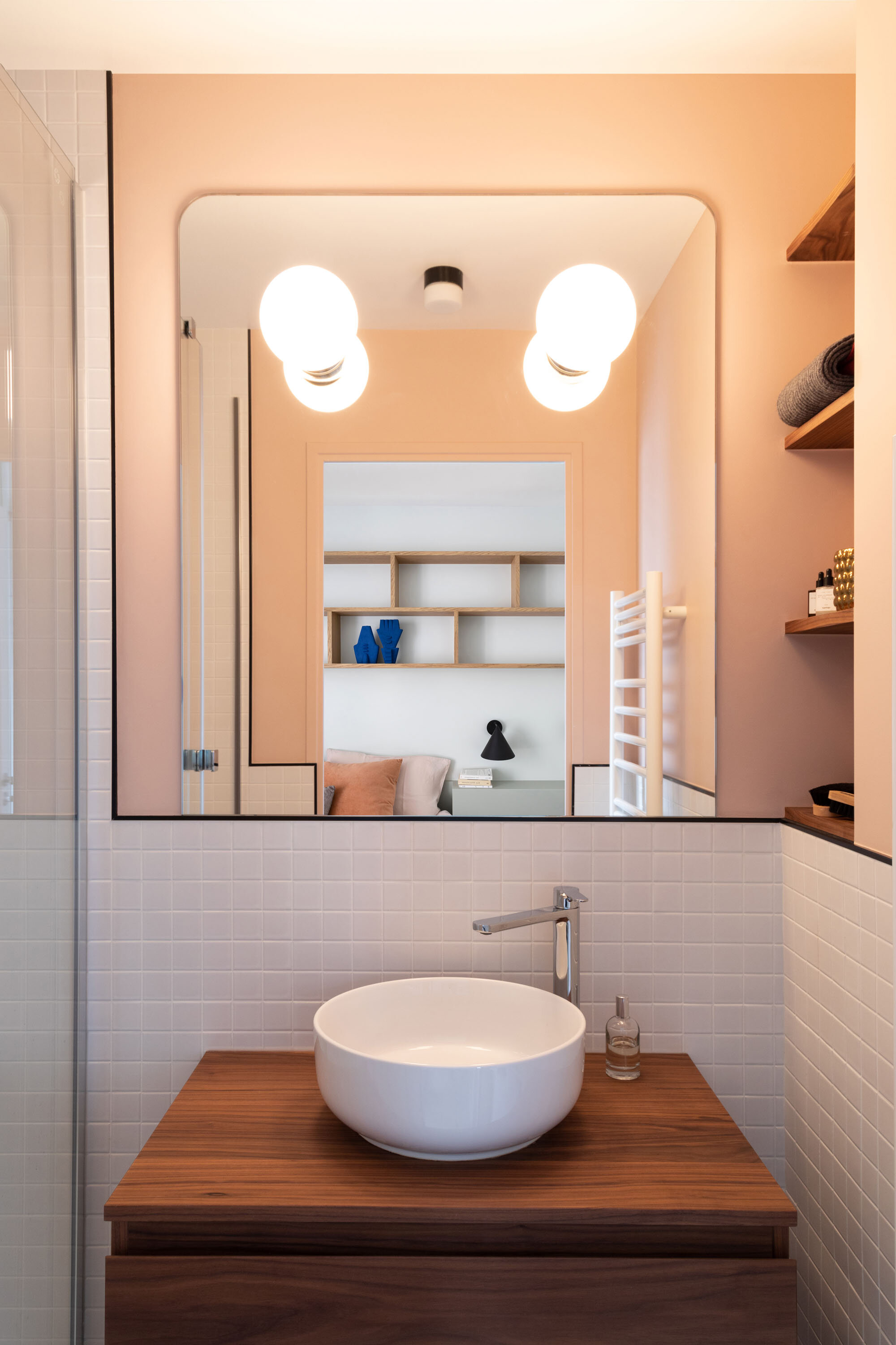 Salle d'eau rose avec un meuble en noyer et un miroir arrondi