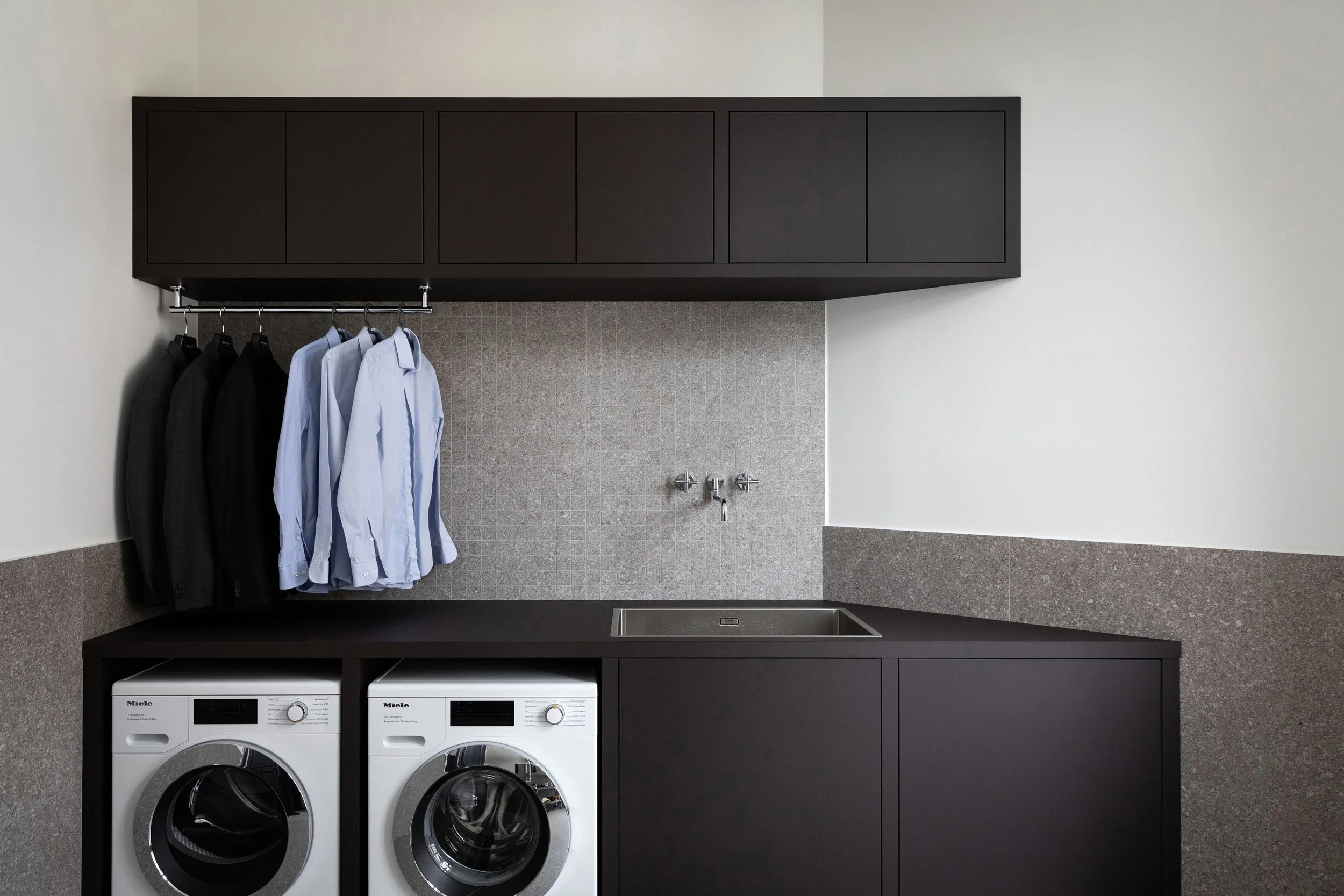 Buanderie sur mesure avec rangements en bois sombre, lave-linge et sèche-linge intégrés