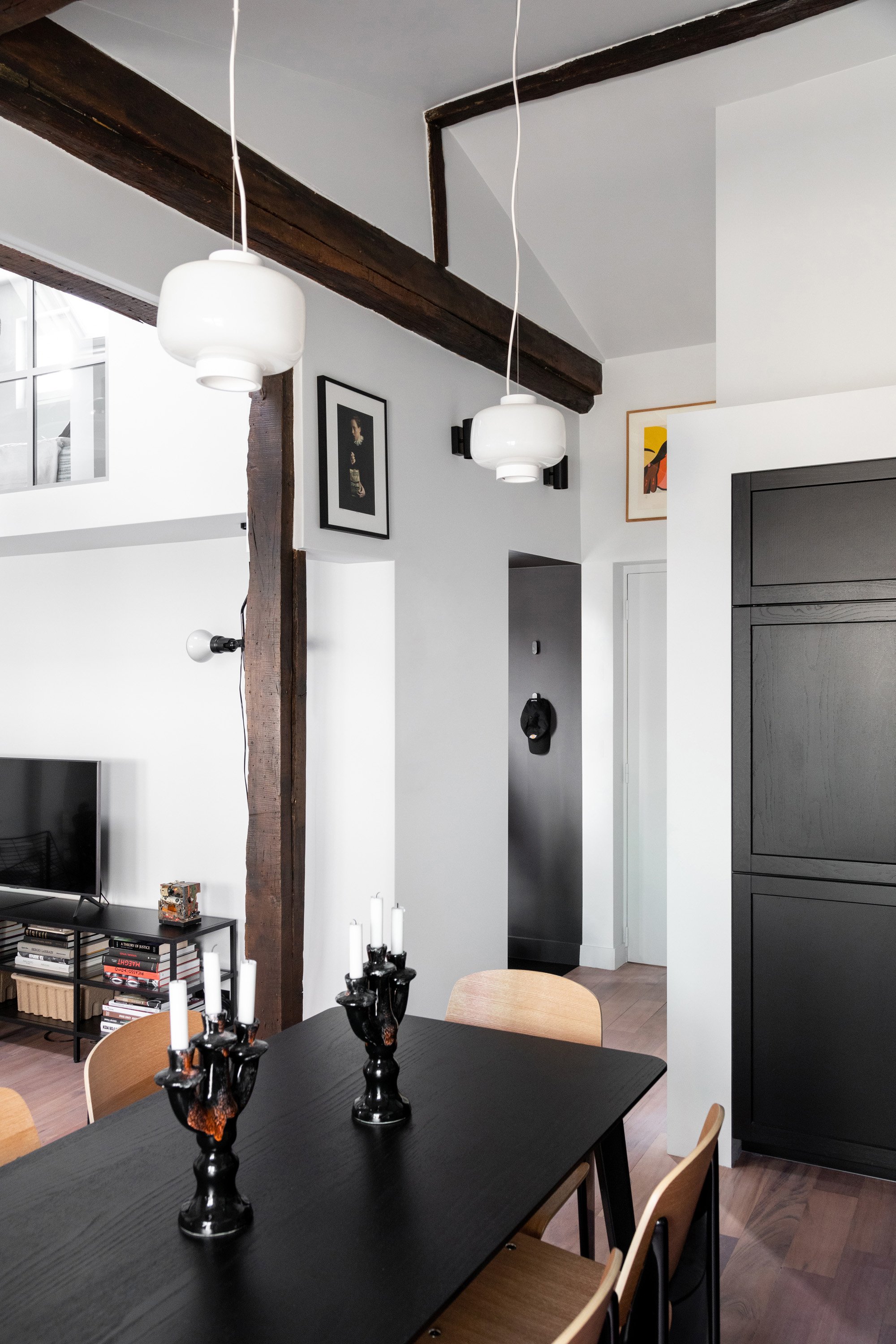 Salle à manger avec table noire et poutres anciennes dans un appartement rénové à Saint-Georges