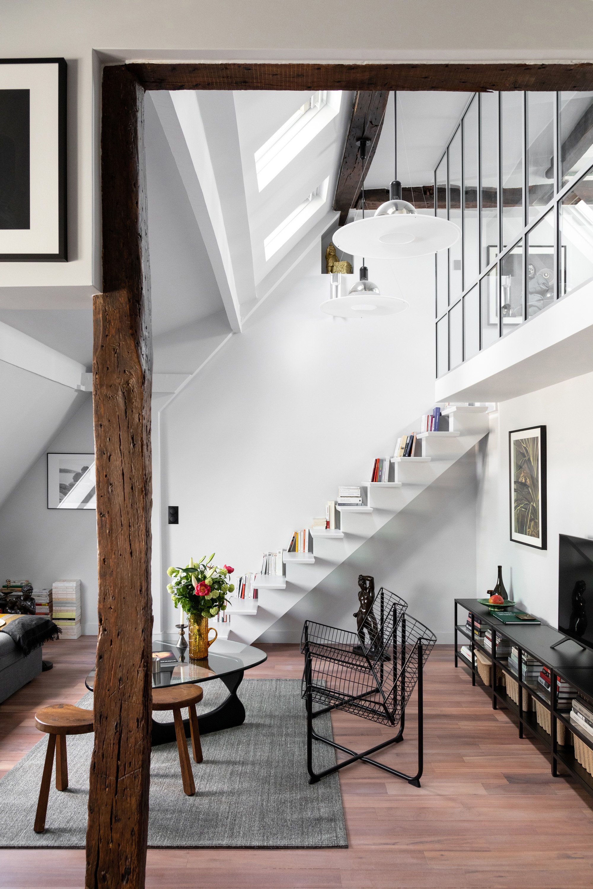 Séjour sous les toits avec escalier, verrière et poutres anciennes dans un appartement rénové à Paris 9