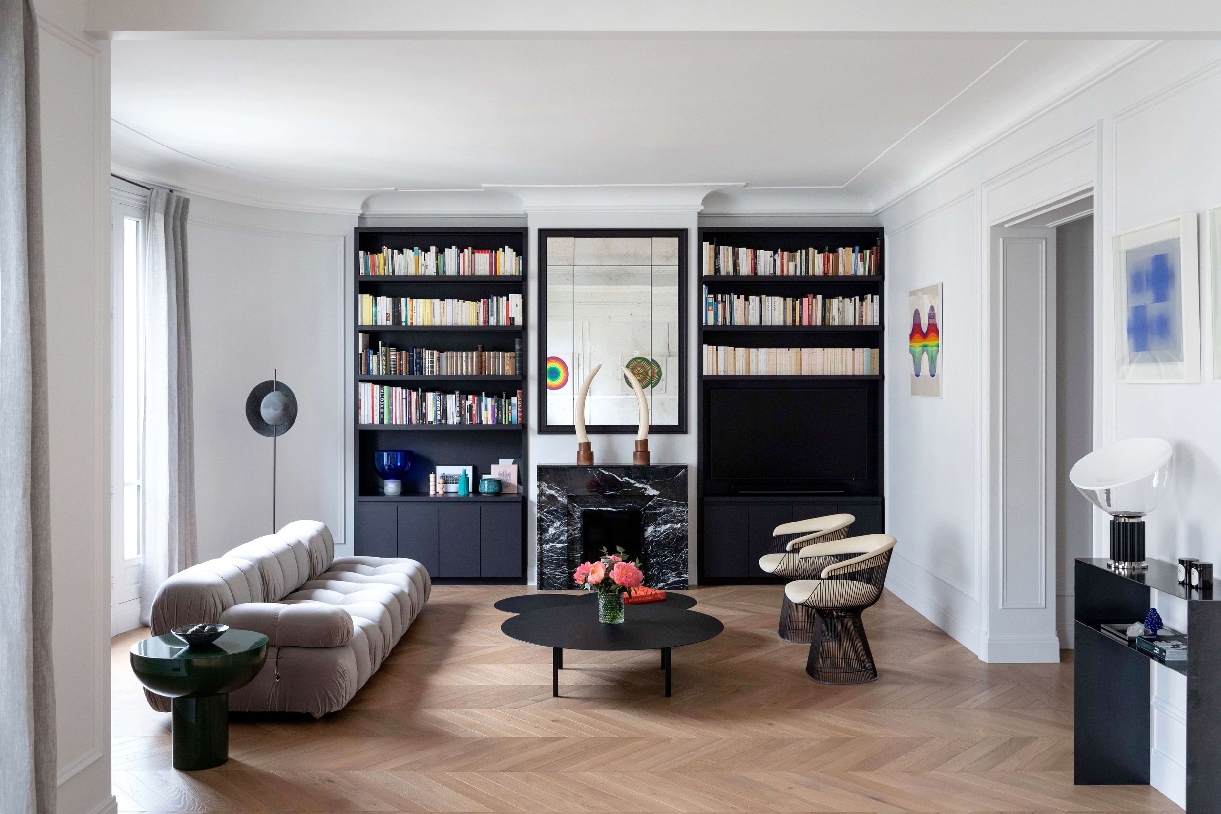 Salon d’un appartement haussmannien rénové à Paris 16 avec cheminée en marbre noir et bibliothèque sur mesure