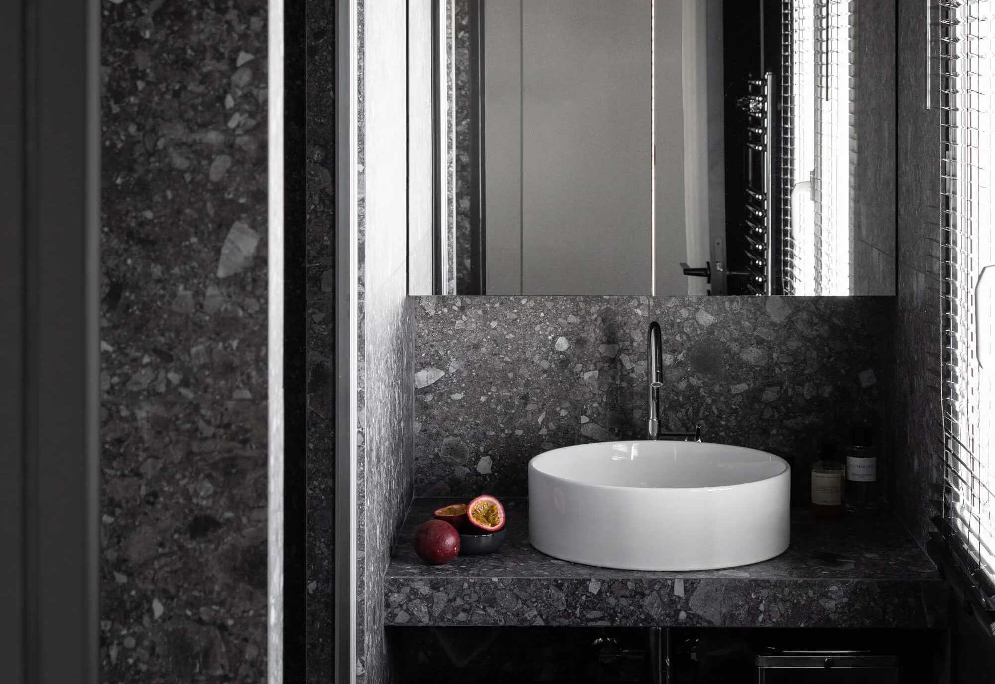 Une salle de bain en gré cérame aux ton noirs et sombres avec une vasque à poser blanche