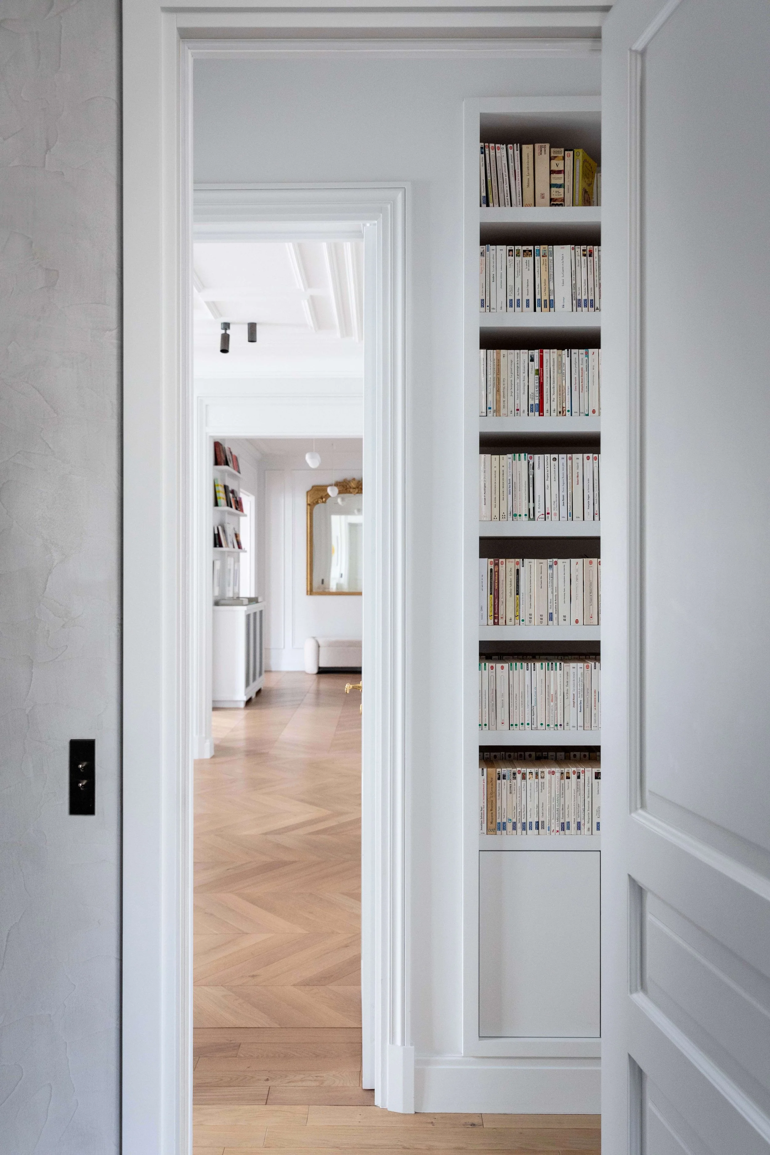 Bibliothèque sur mesure intégrée dans un passage entre les pièces d’un appartement rénové à Paris 16