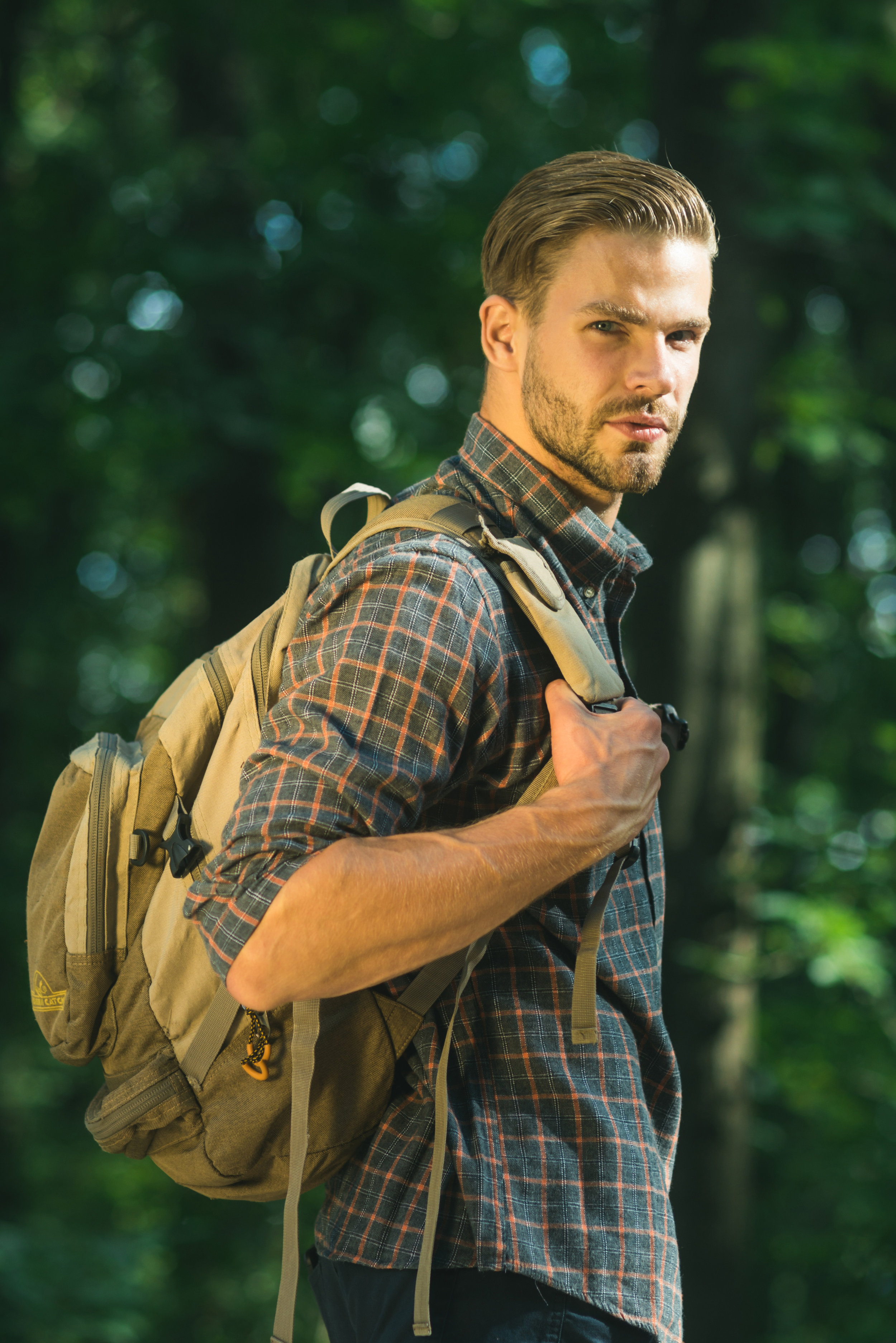 Bearded hipster hiking holiday, wild adventure. Young man hiking in forest and breathes pure air on sunny day - concept of clean air and healthy lifestyle.