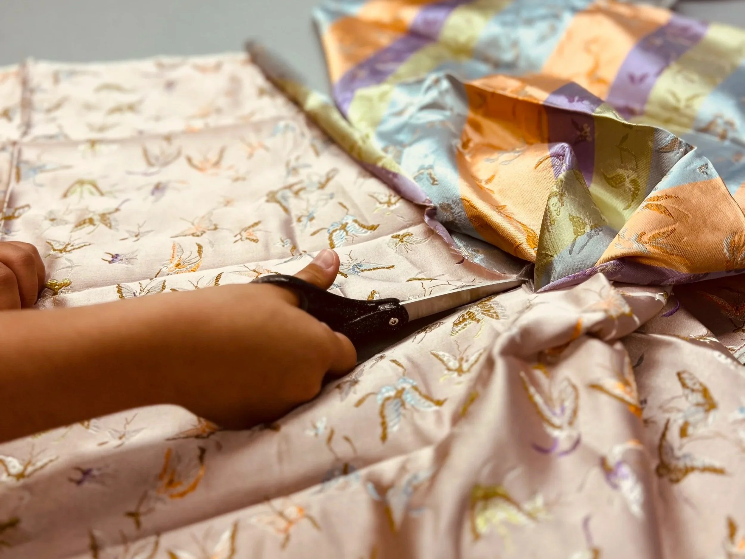 cutting chinese damask satin in peach and gold colors with black scissors