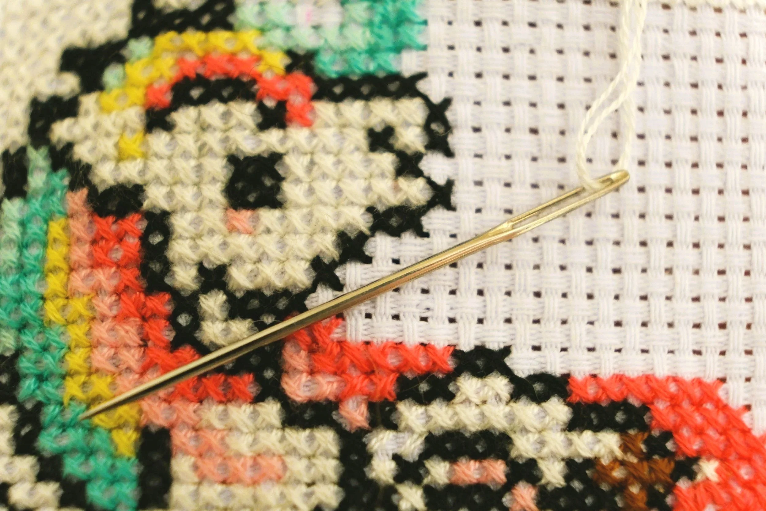 cross-stitch pattern in orange and black with a golden needle