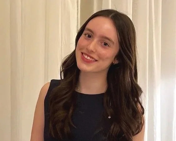Brunette teen girl with long hair and black top, smiling