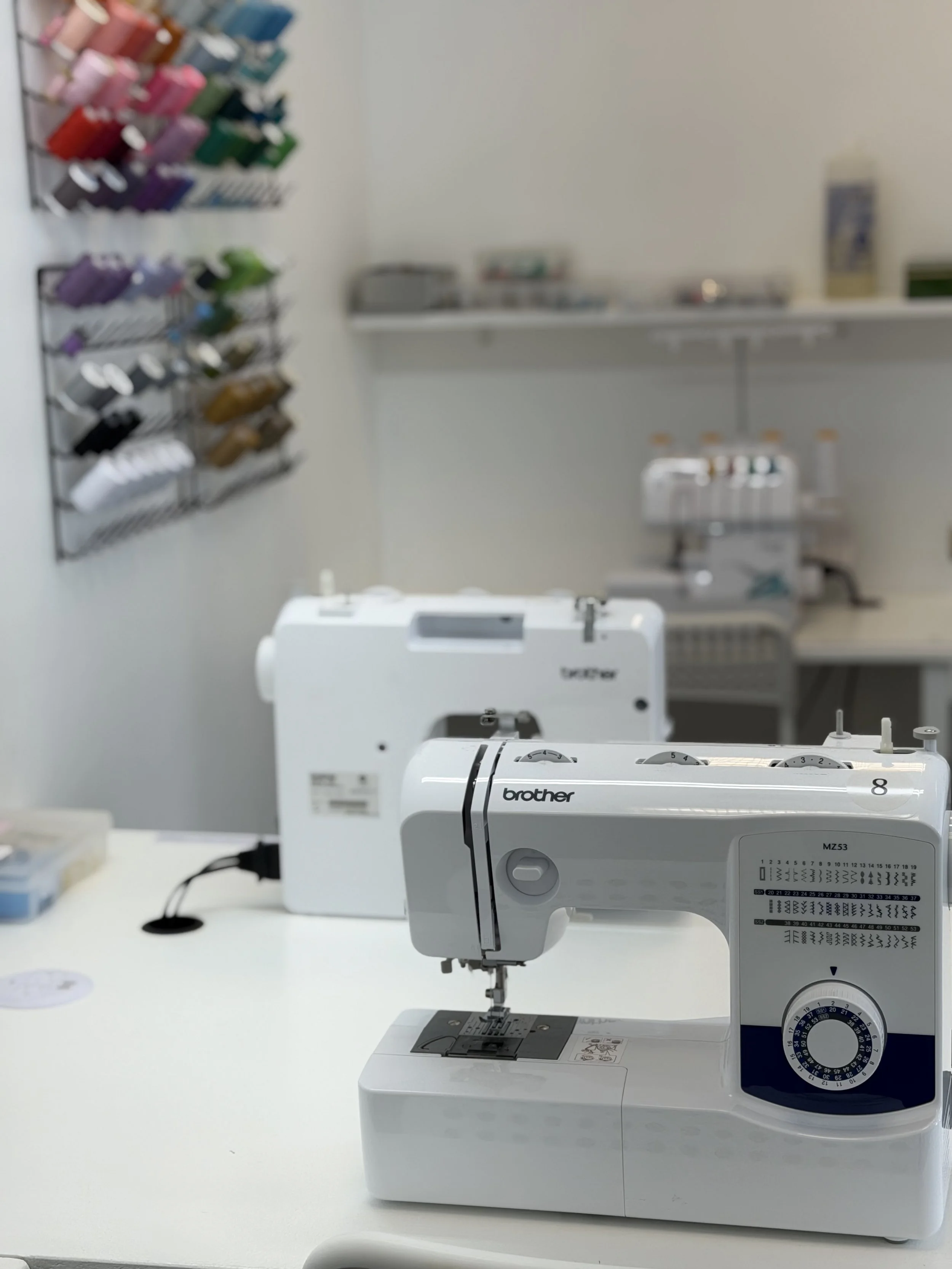 white brother machine in front and back on a white table, threads multicolored on the wall