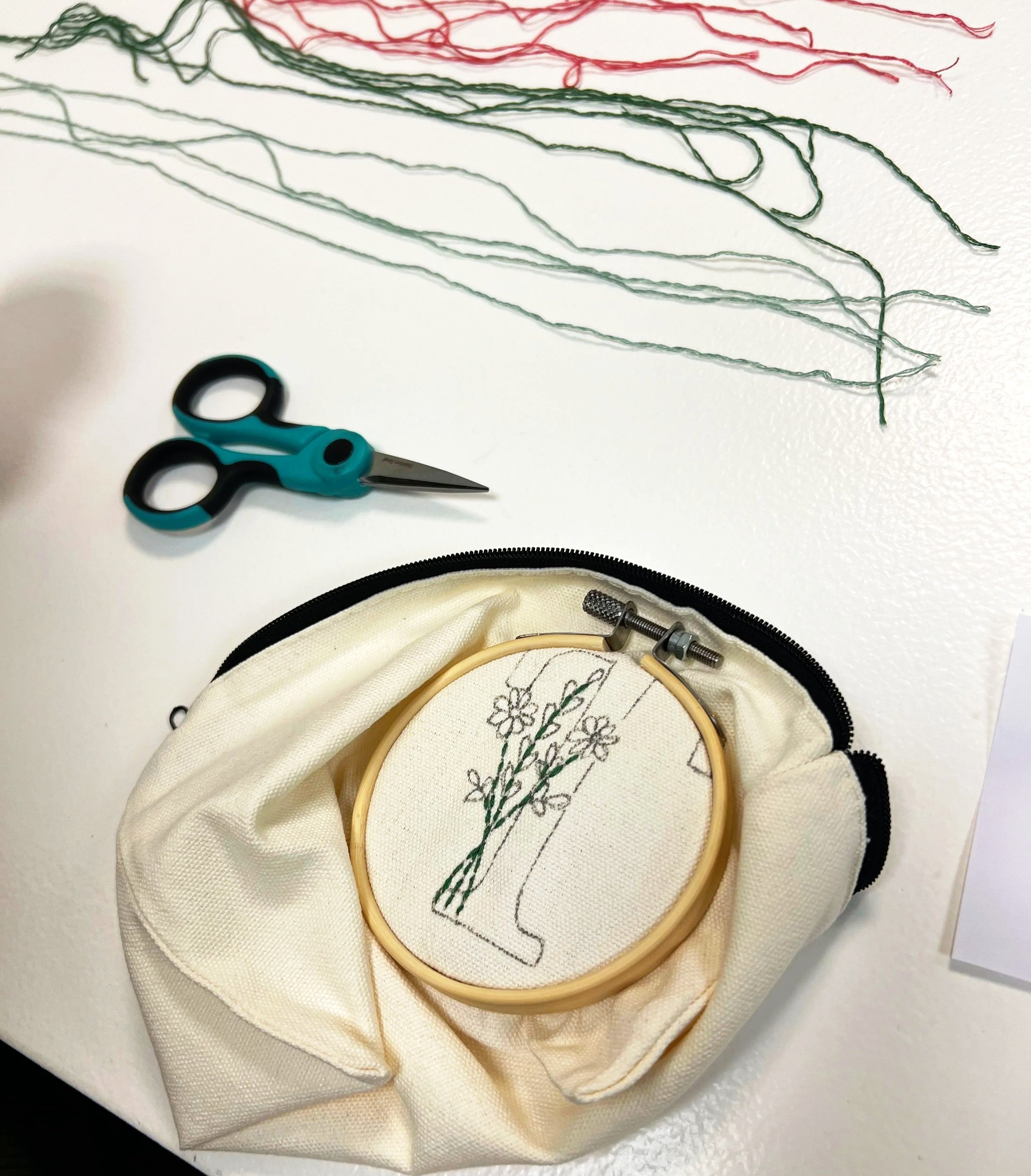 muslin fabric in an embroidery hoop with hand embroidered letter T and flowers, a pair of detail scissors and floss